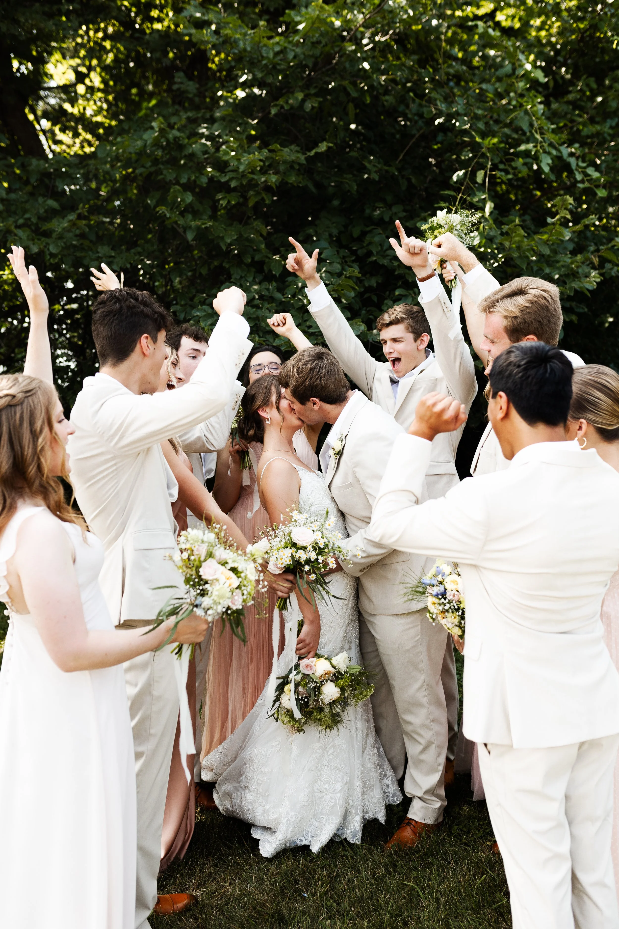 A wedding celebration with a bride and groom kissing surrounded by friends, who are celebrating and cheering.