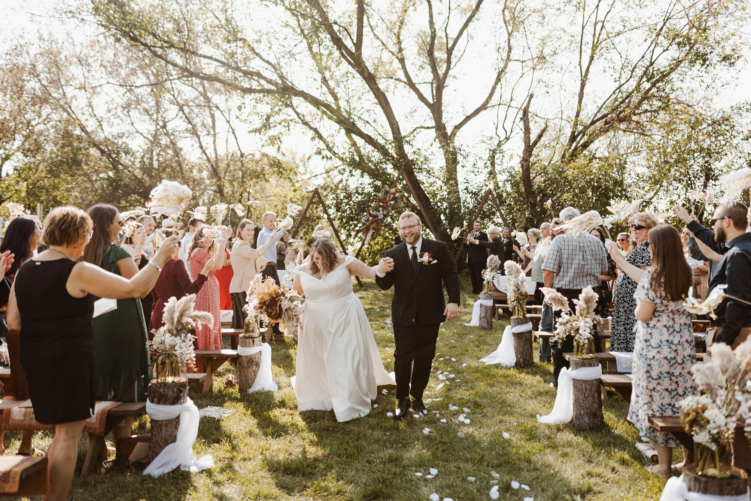 Bride and groom walking hand in hand down the aisle at an outdoor wedding ceremony, surrounded by celebrating guests throwing flower petals