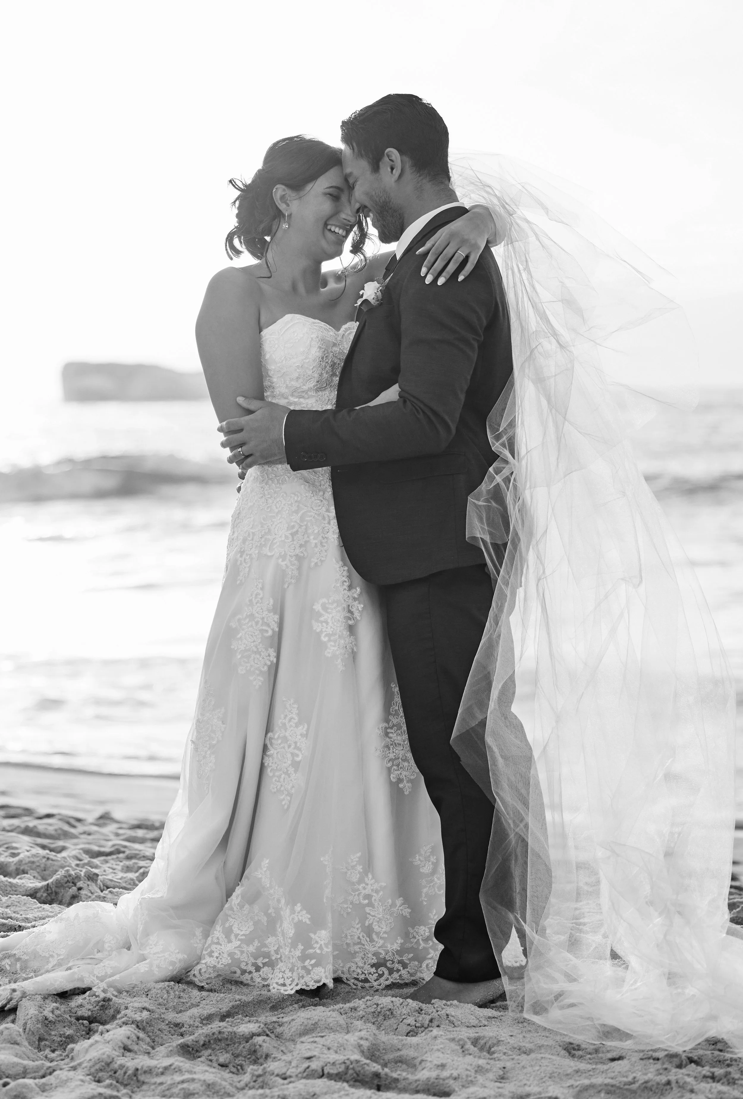 A bride and groom embracing on the beach after their wedding.