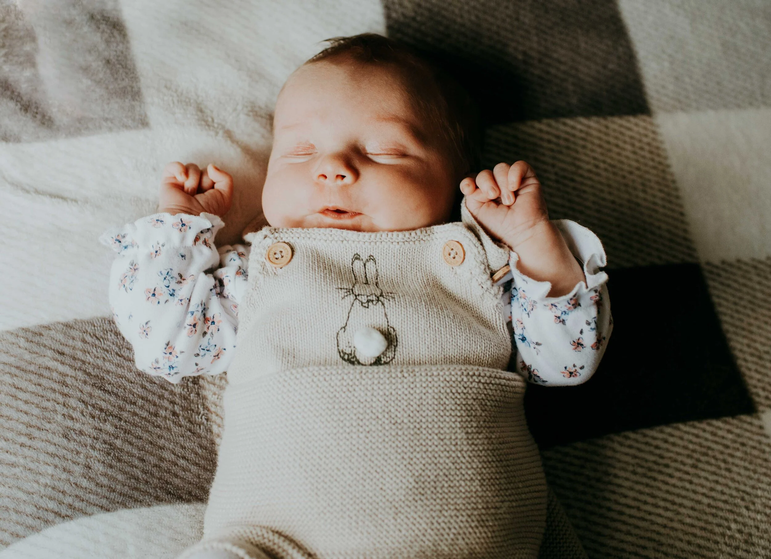 Sleeping baby in knitted outfit with bunny design on a plaid blanket.