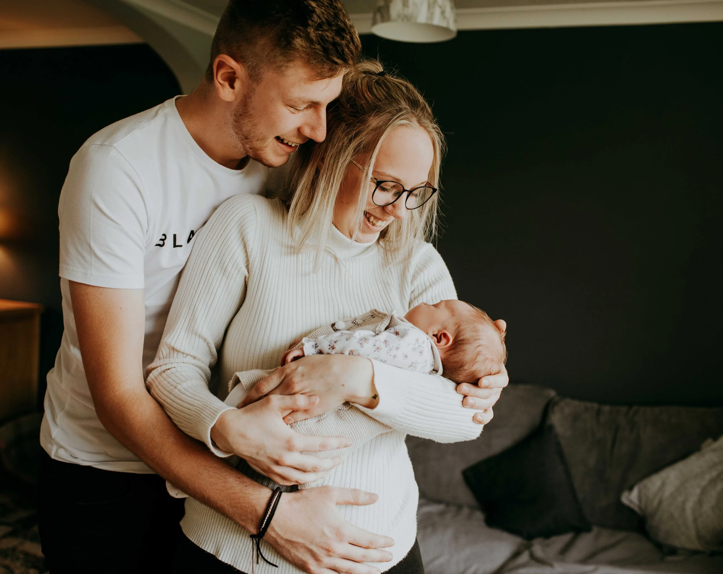 A couple smiling and cuddling a baby indoors.