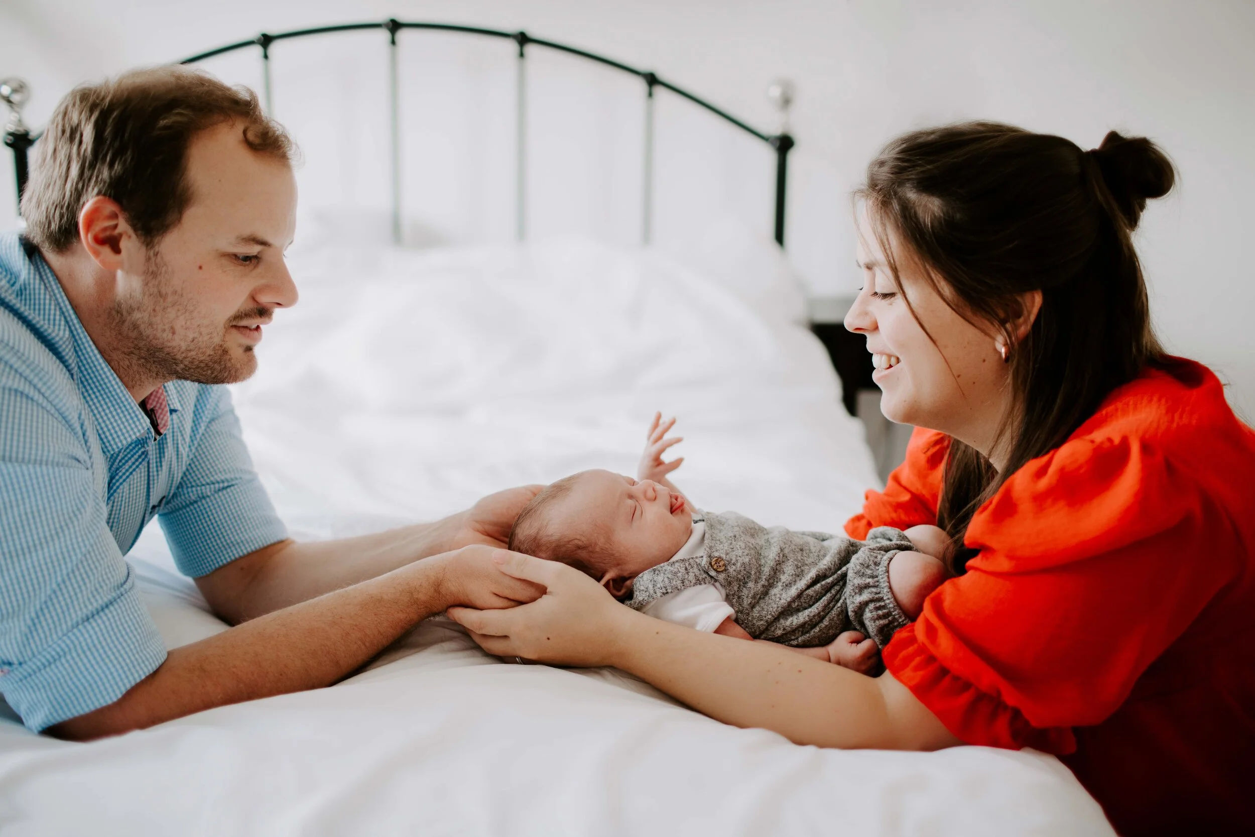 Parents with baby on bed, smiling and engaging with the infant.