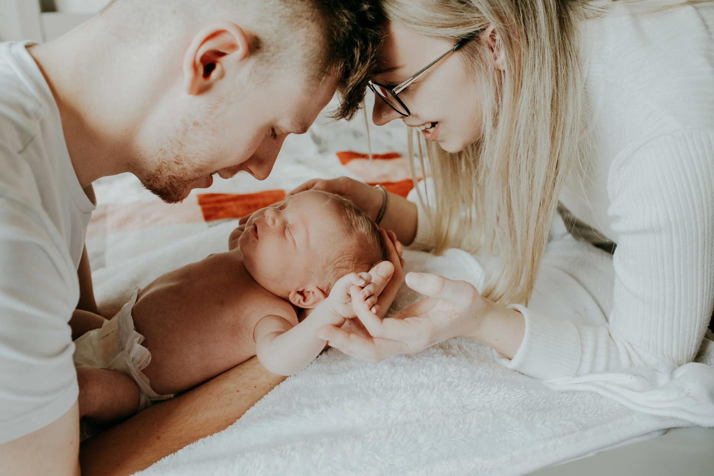 Parents bonding with newborn baby on bed, close-up shot.
