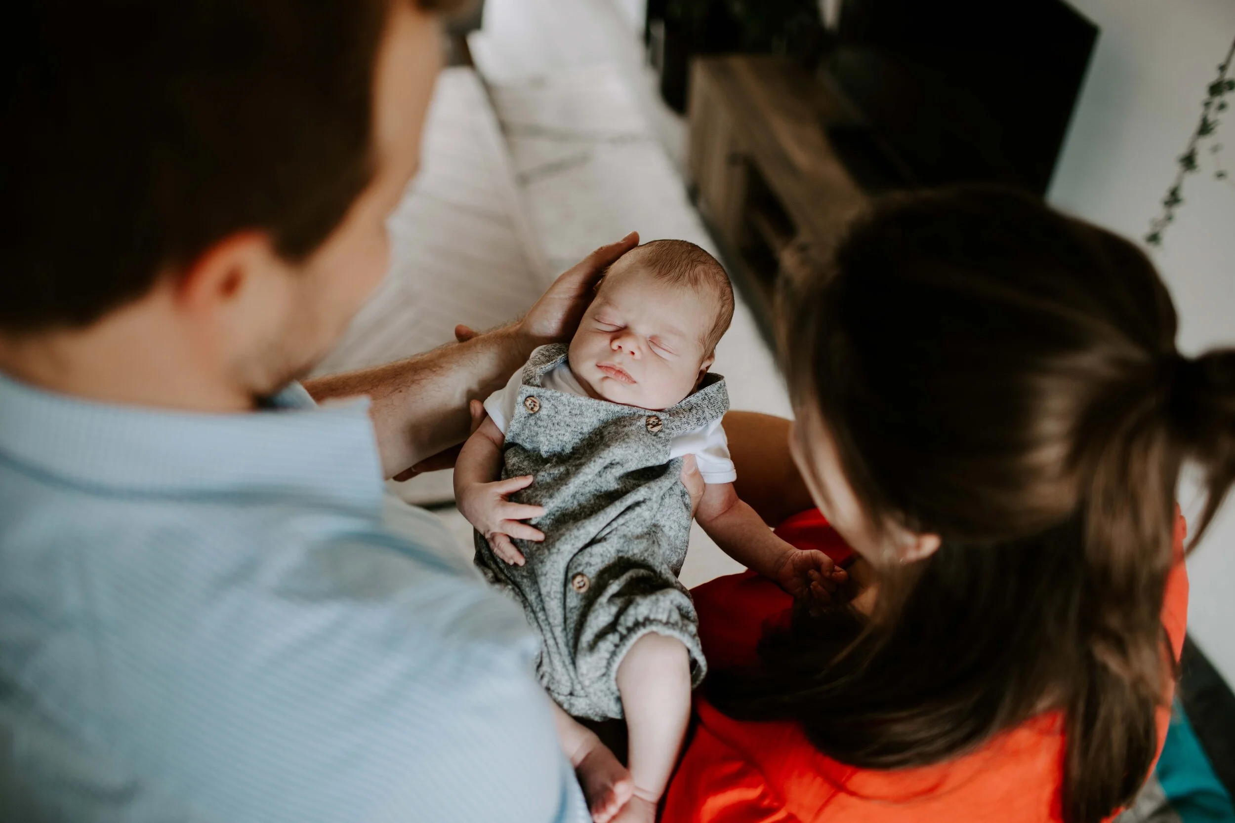 Parents holding a sleeping newborn in a gray outfit.