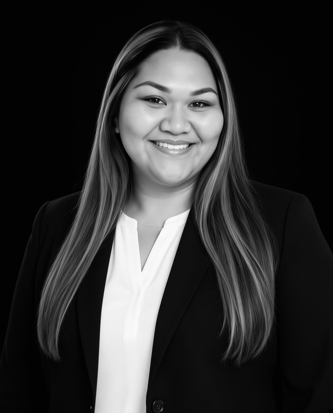Black and white professional headshot of a smiling woman with long hair, wearing a suit and white blouse against a dark background.
