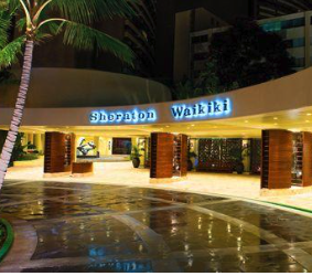 Entrance sign for shopping at Shoppoon Waikiki with lights and palm trees at night