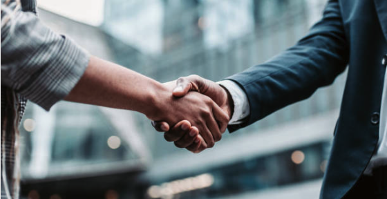 Close-up of two people shaking hands in an office setting with modern glass buildings in the background.