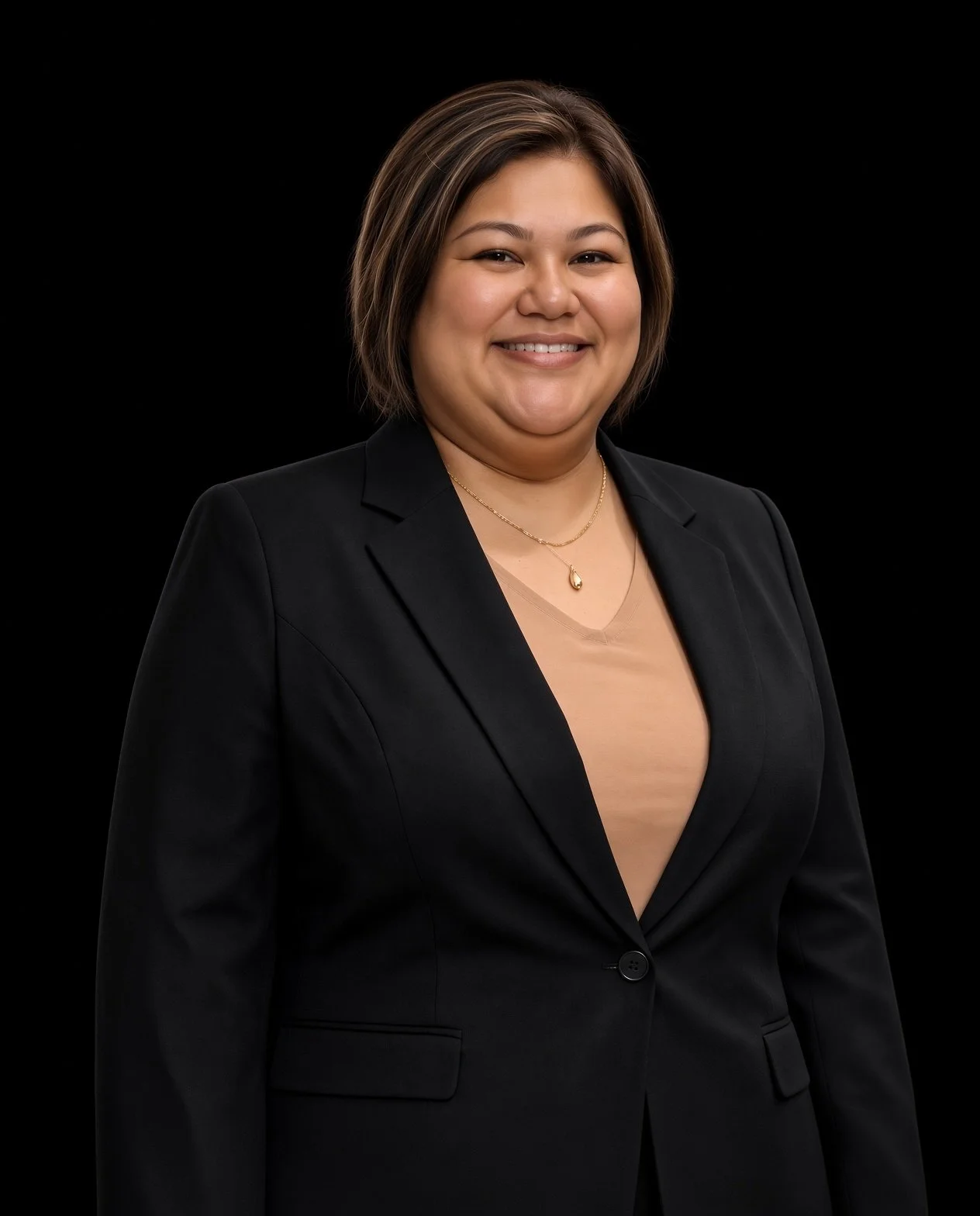 A woman with medium-length brown hair, smiling, dressed in a black blazer over a beige top, wearing a gold necklace, against a black background.