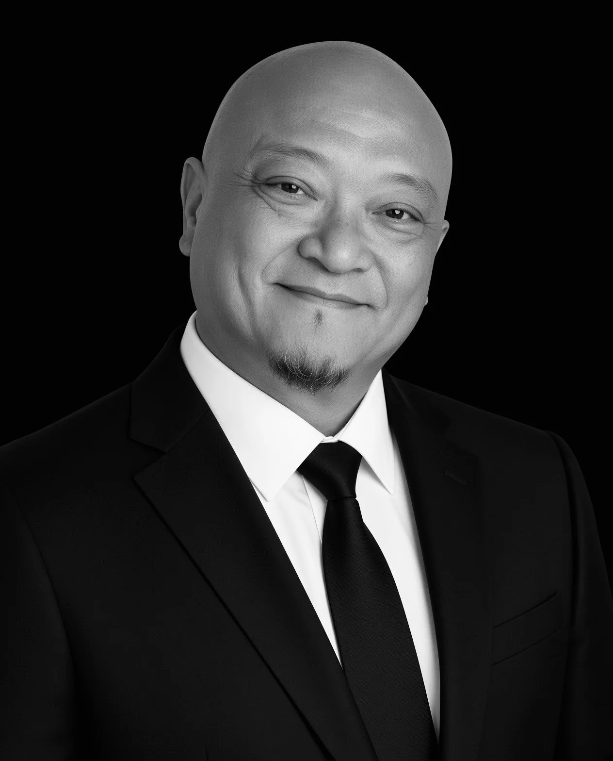 Black and white portrait of a smiling man in a suit and tie with a bald head and goatee.