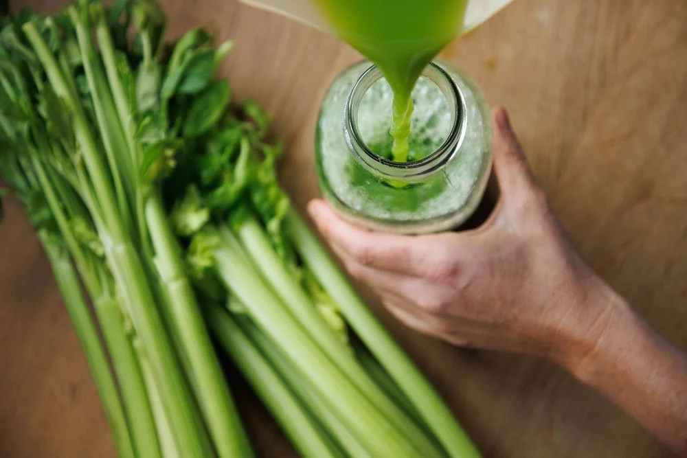 Perspektive von oben: Frisch gepresster Sellerie wird in einen Flasche gegossen, Stangensellerie im Hintergrund