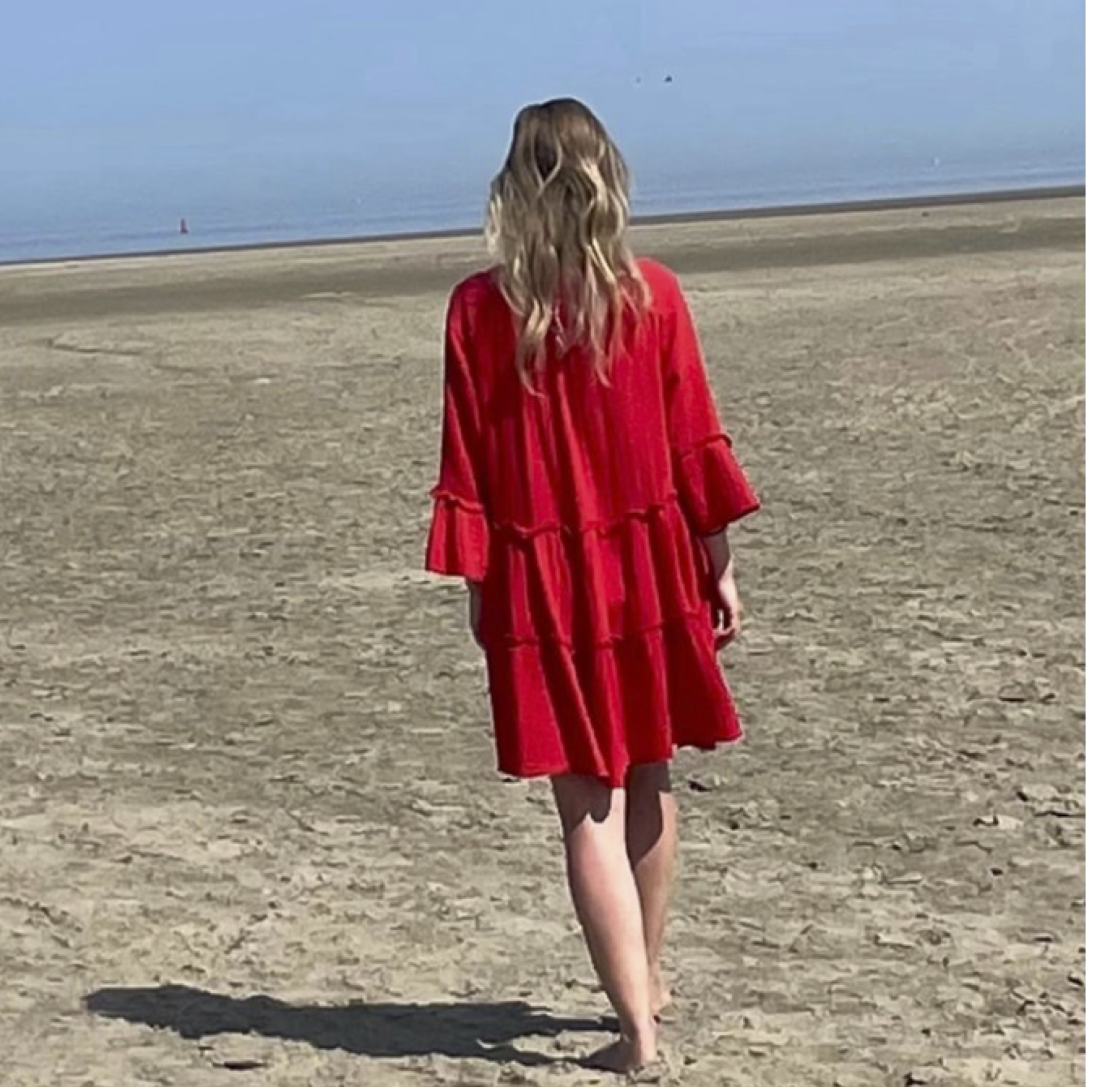 Maartje walking on the beach in a red dress.
