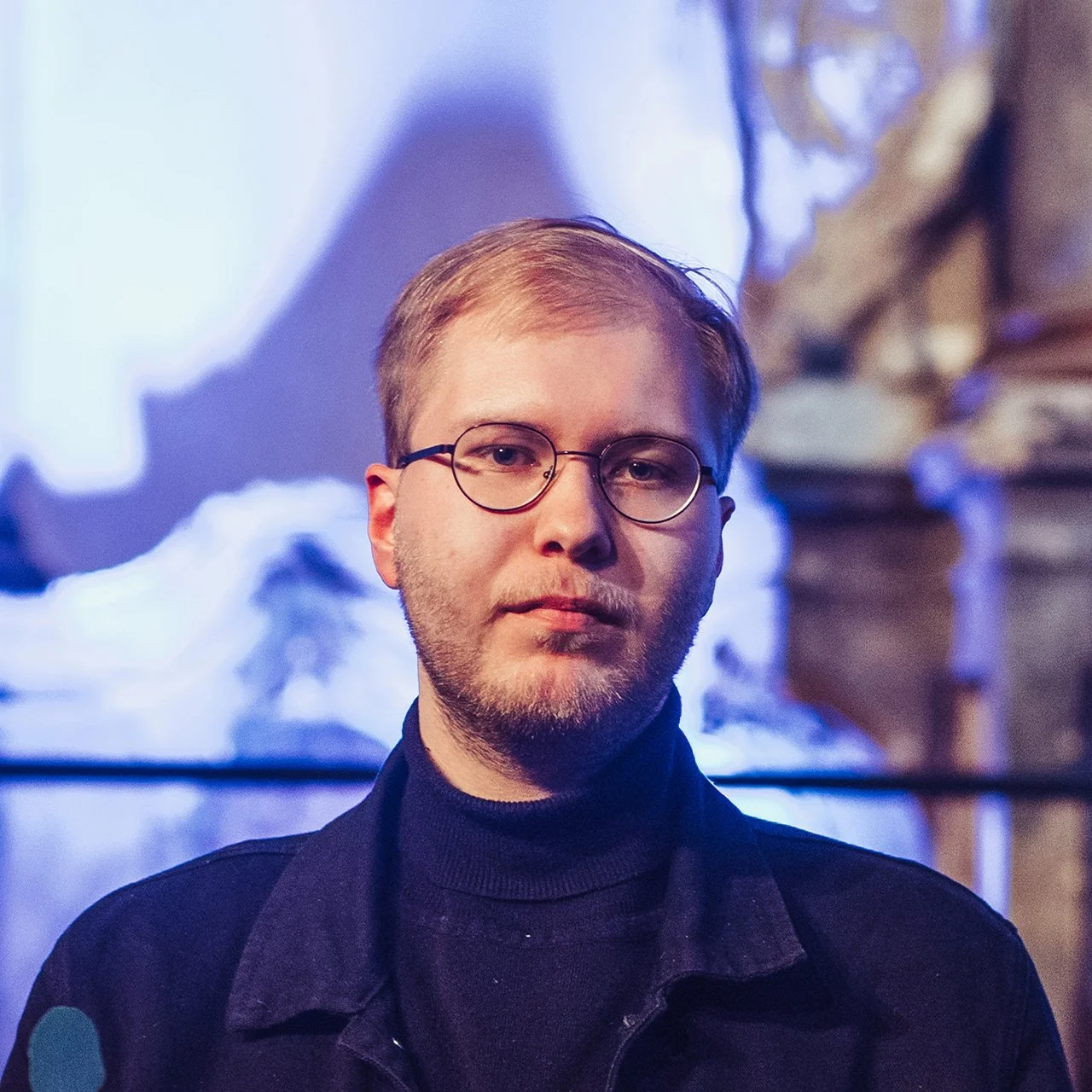 Photograph of Lukas Butkus, a young white man with blonde hair and a neat beard wearing glasses