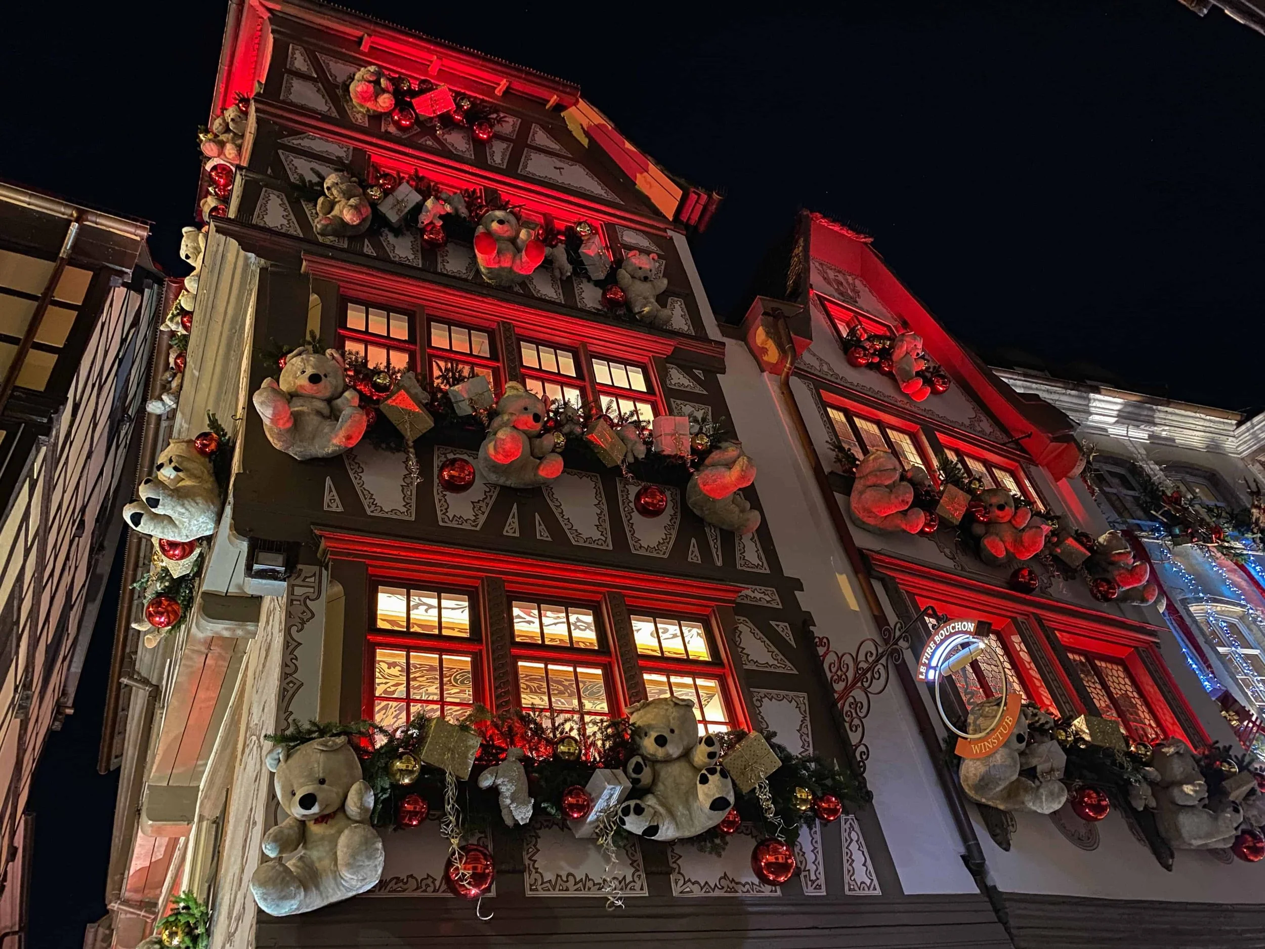 Half-timbered Strasbourg building lit in red and covered in teddy bears and ornaments at night