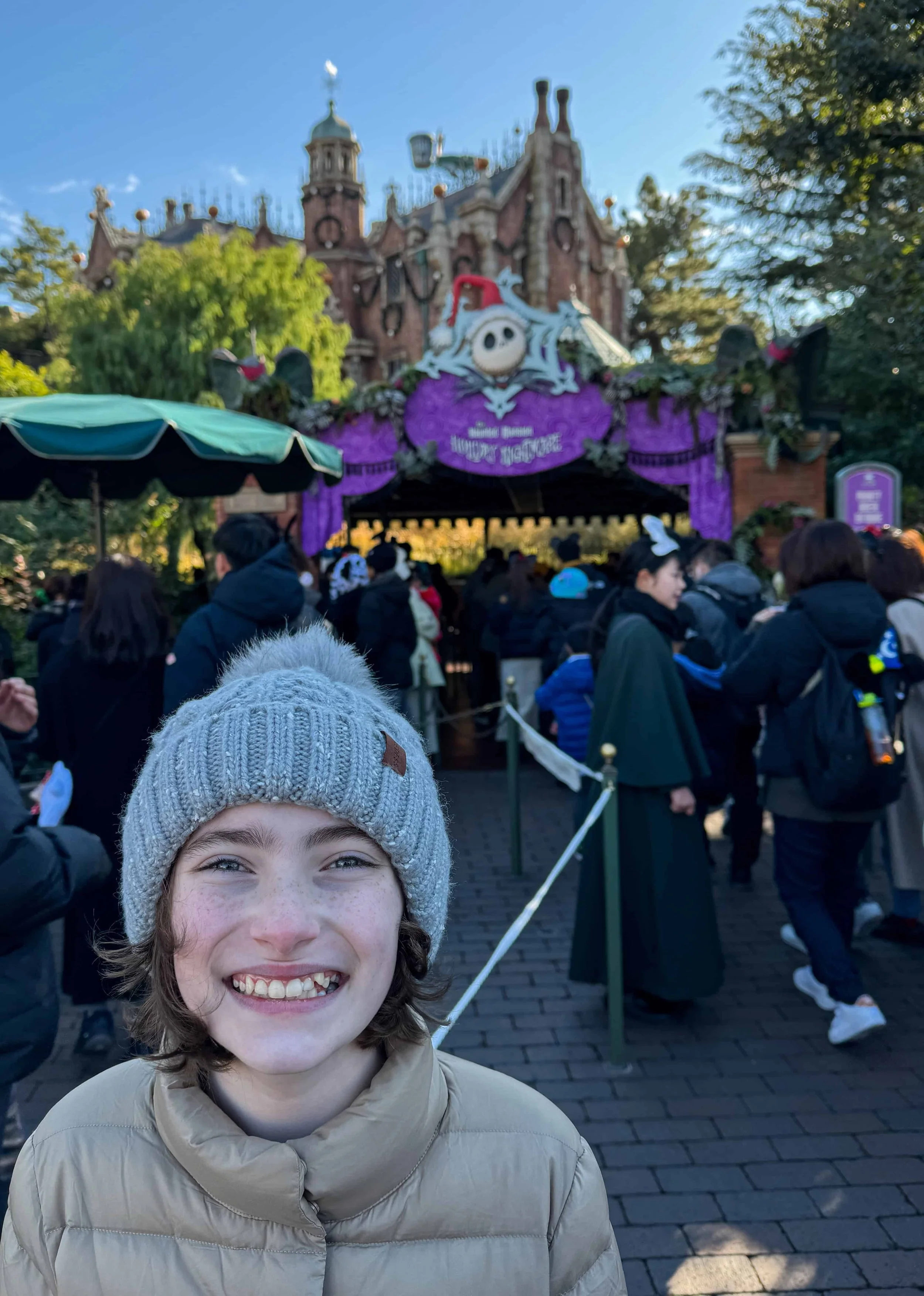 A family member in a gray pom-pom beanie smiles in the Haunted Mansion Holiday Nightmare queue
