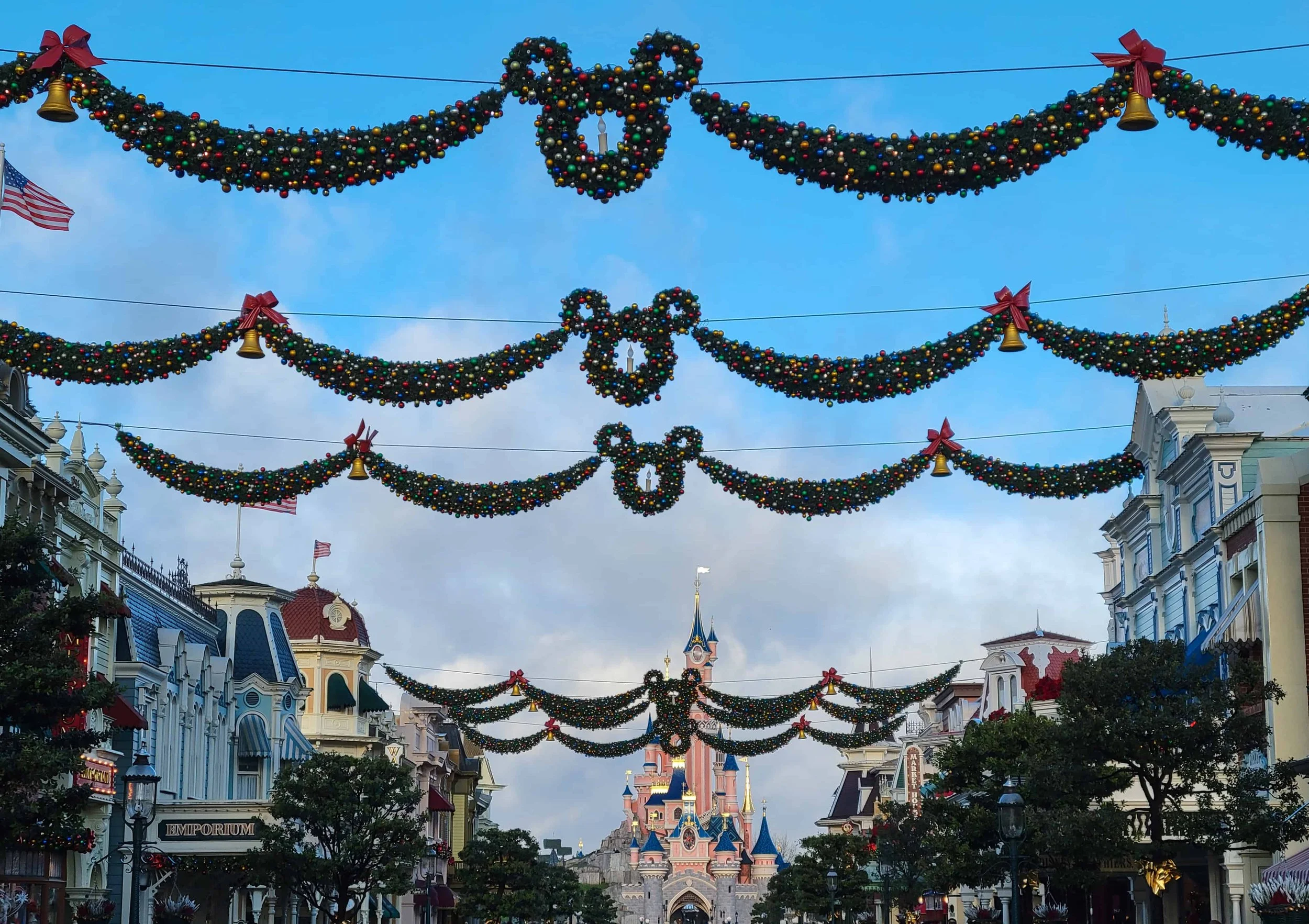 Christmas garlands with Mickey-shaped wreaths hang across Main Street, U.S.A., with Sleeping Beauty Castle in the distance.