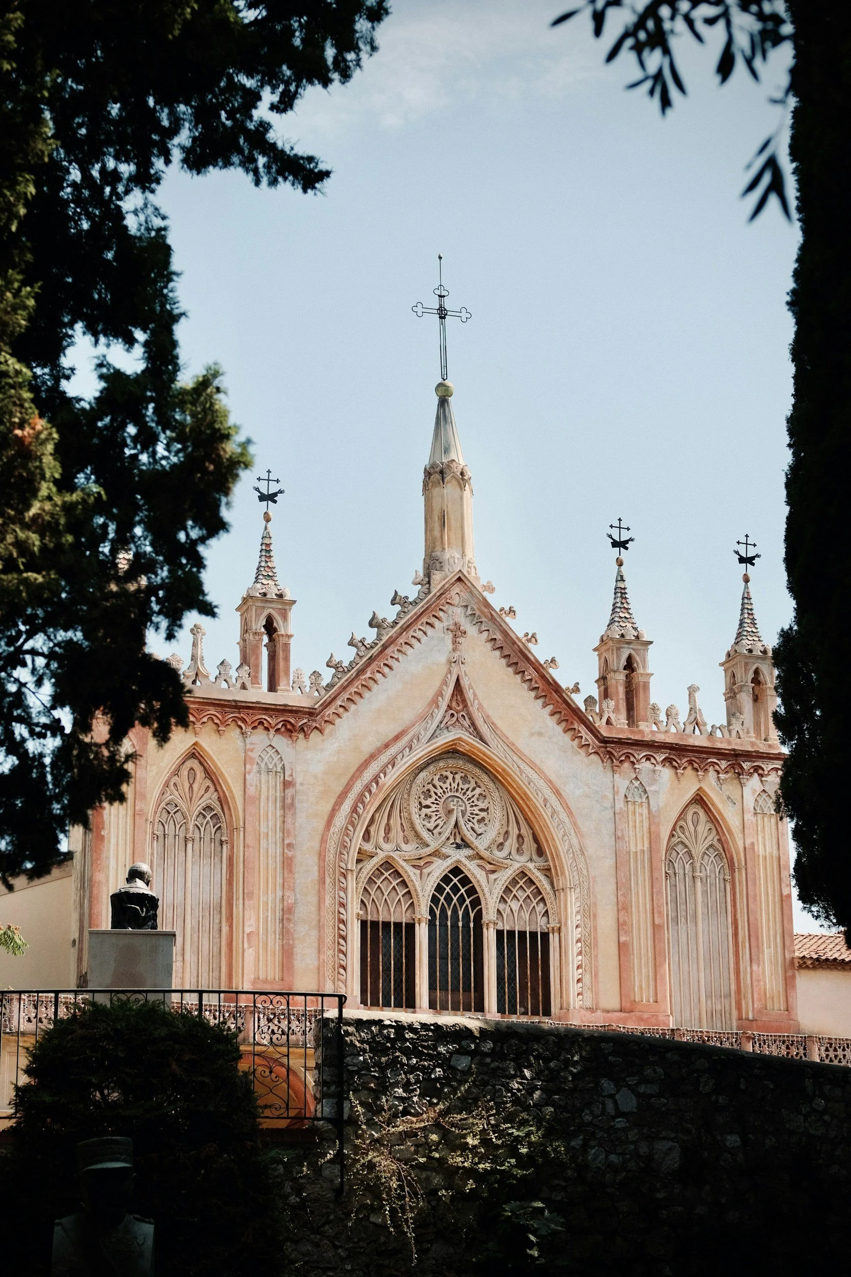 Gothic facade of the Cimiez Monastery in Nice, France — ornate pink stone church with spires and a small statue visible in the garden below