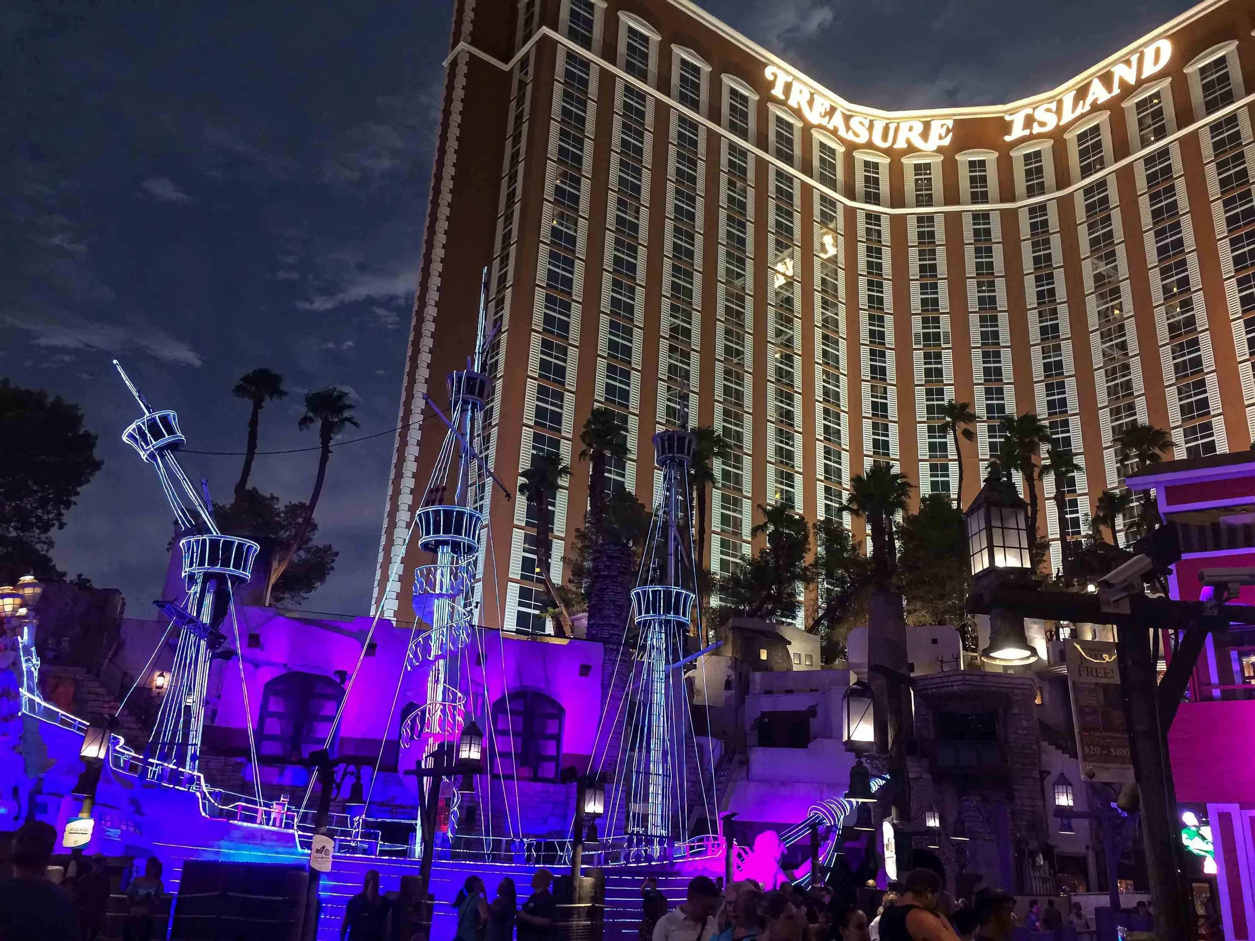 A nighttime picture of Treasure Island Hotel with a lighted pirate ship in front.