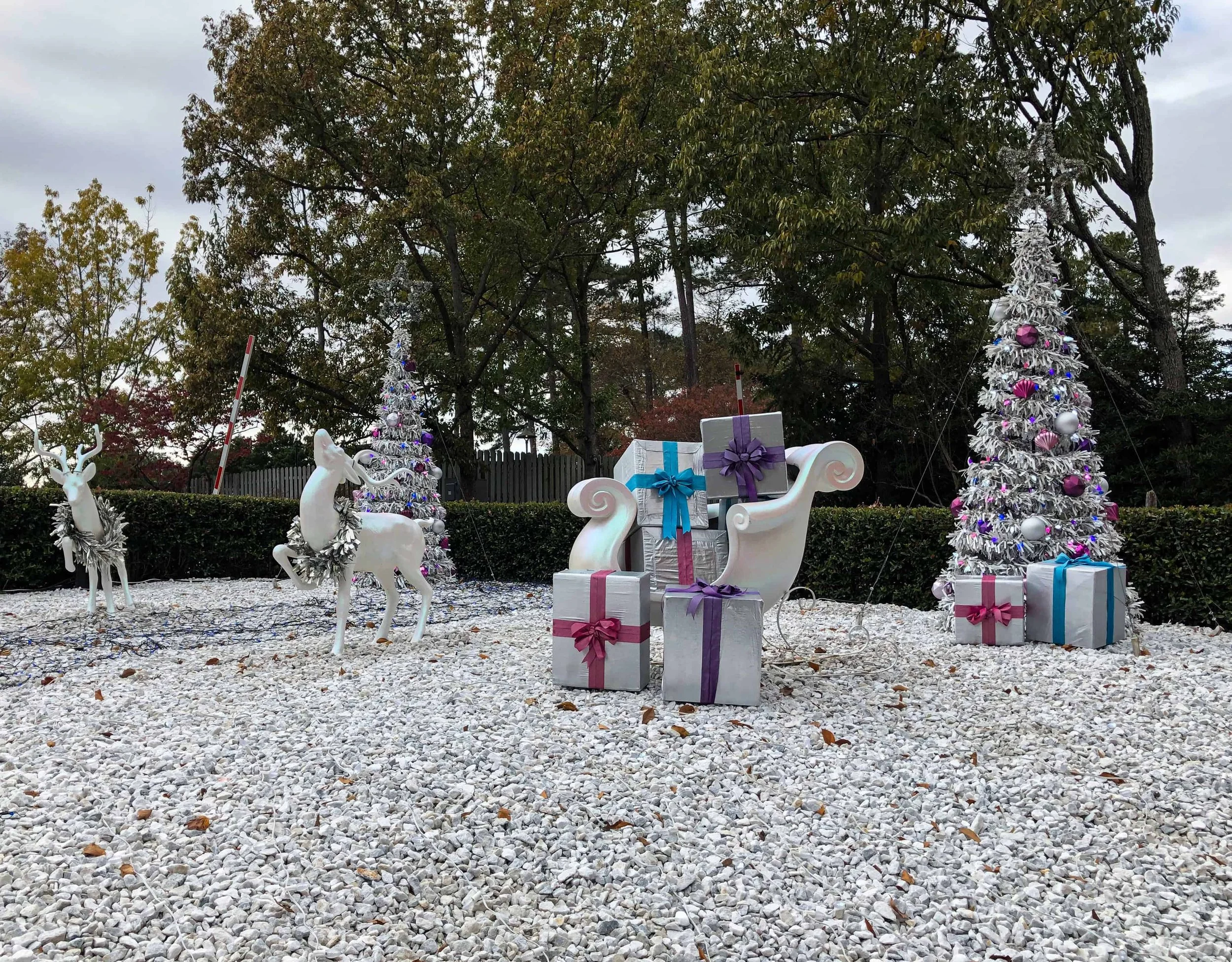 White reindeer, a silver sleigh, wrapped presents, and tinsel Christmas trees on a bed of white gravel.