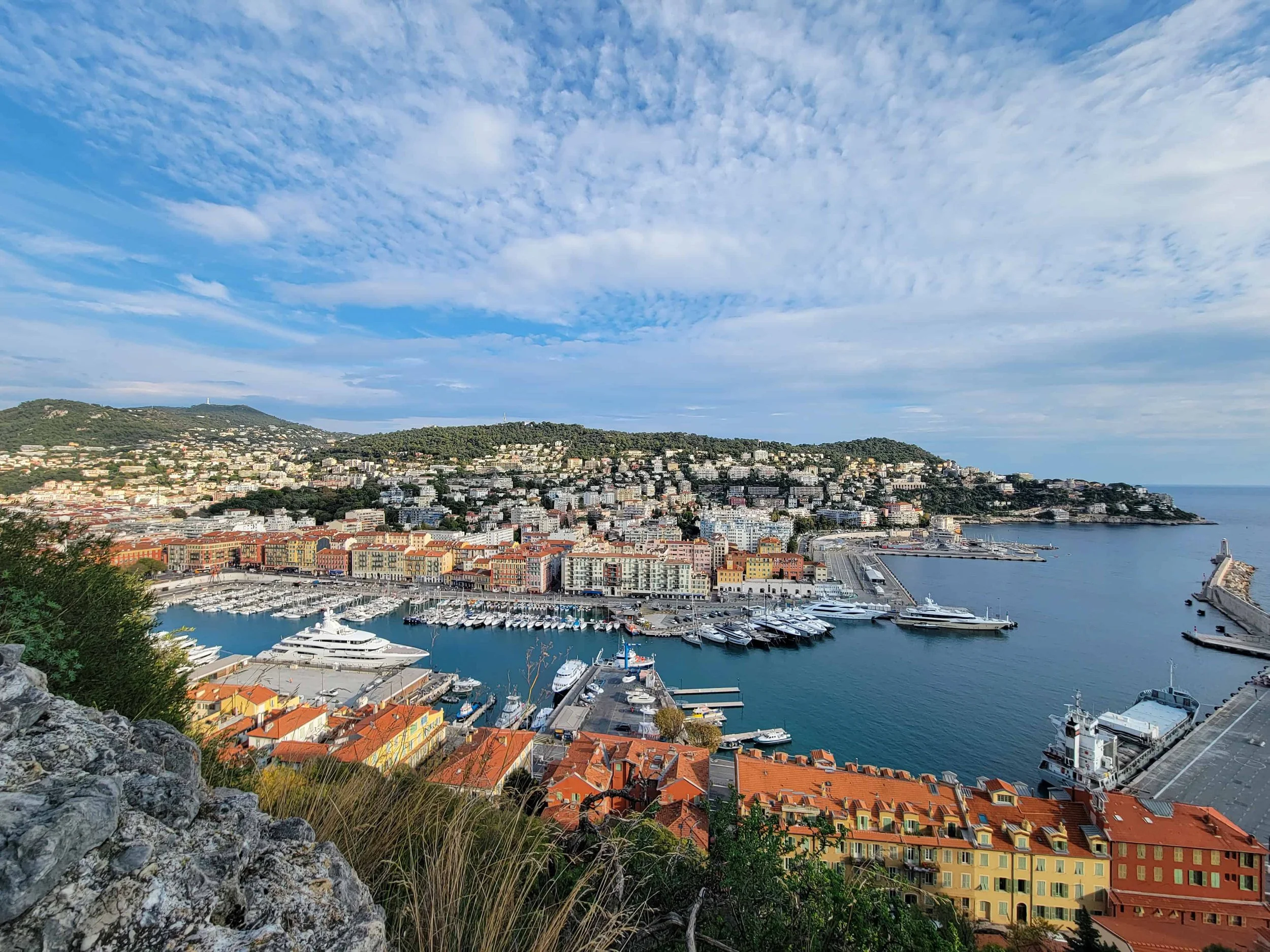 Aerial view from Castle Hill in Nice looking down over Port Lympia, superyachts, terracotta rooftops, and the Mediterranean coastline toward Coco Beach