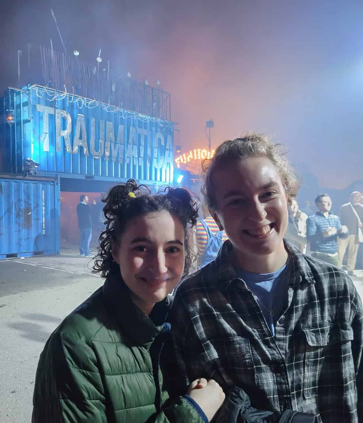 Two family members smiling in the fog near the lit Traumatica entrance sign.