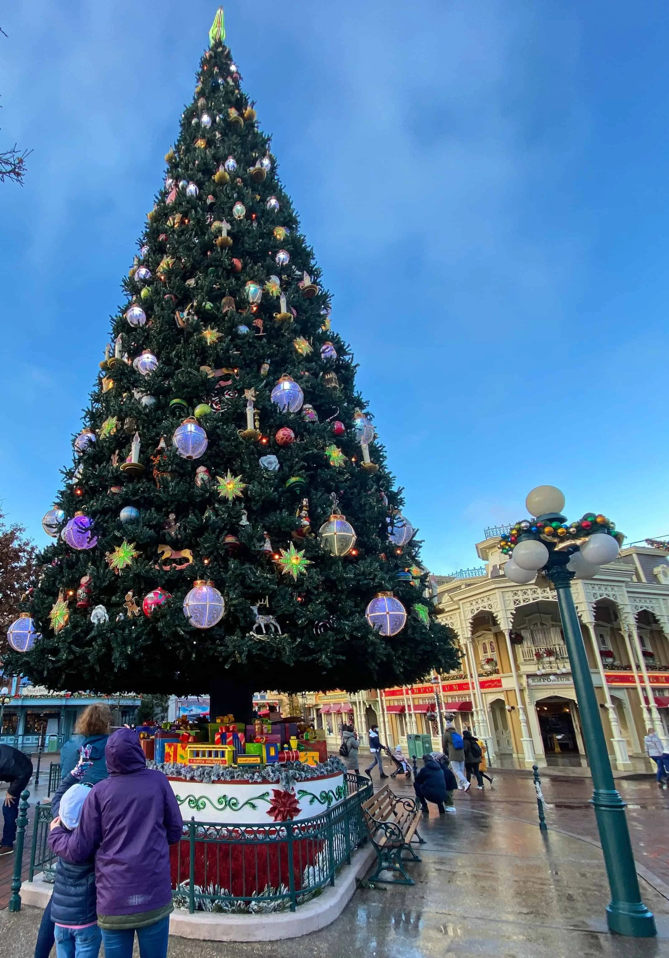 Three family members in winter jackets look up at the giant Christmas tree in Town Square at Disneyland Paris.