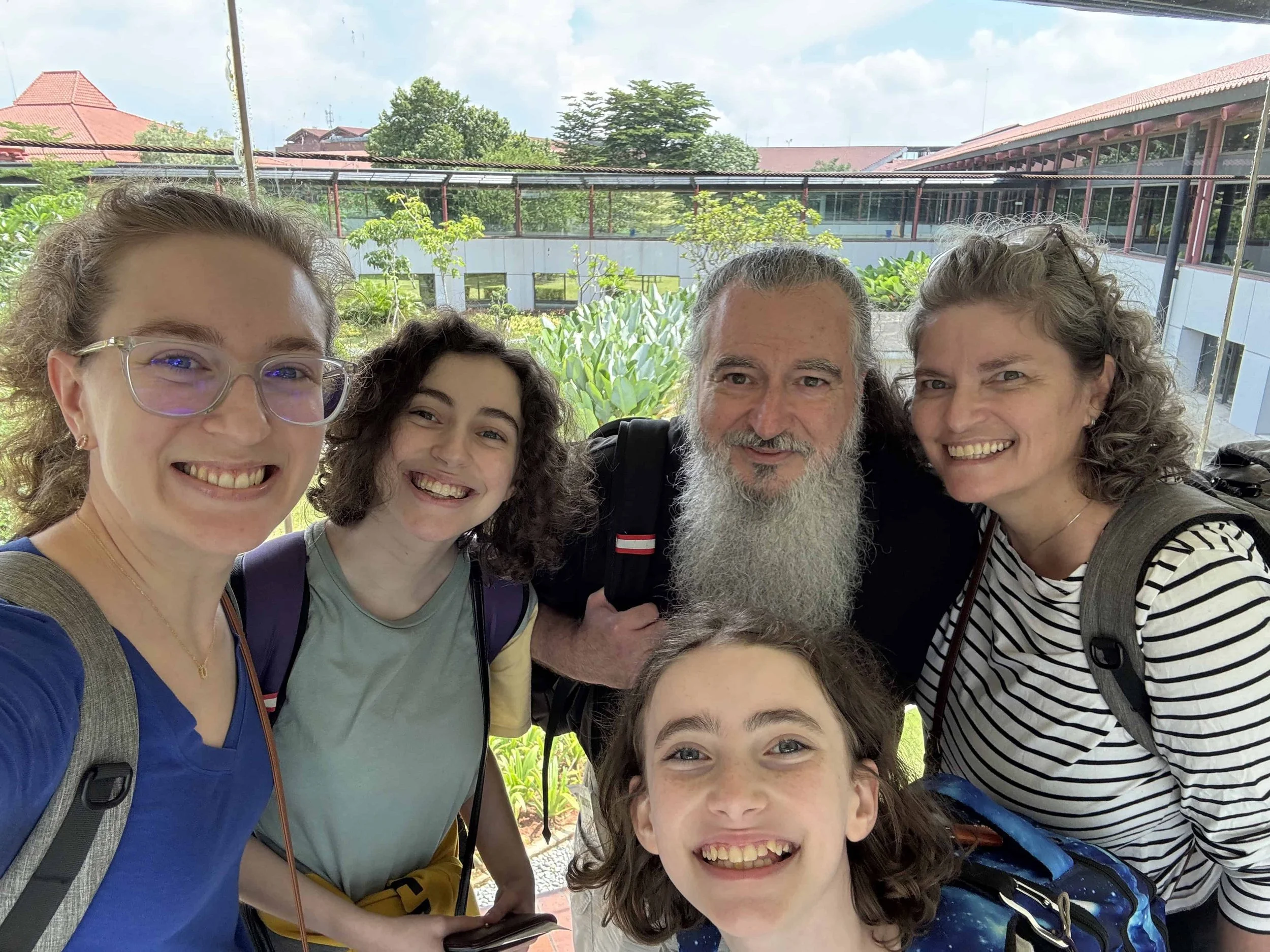 Family of five taking a selfie at Jakarta International Airport with greenery and a building in the background.