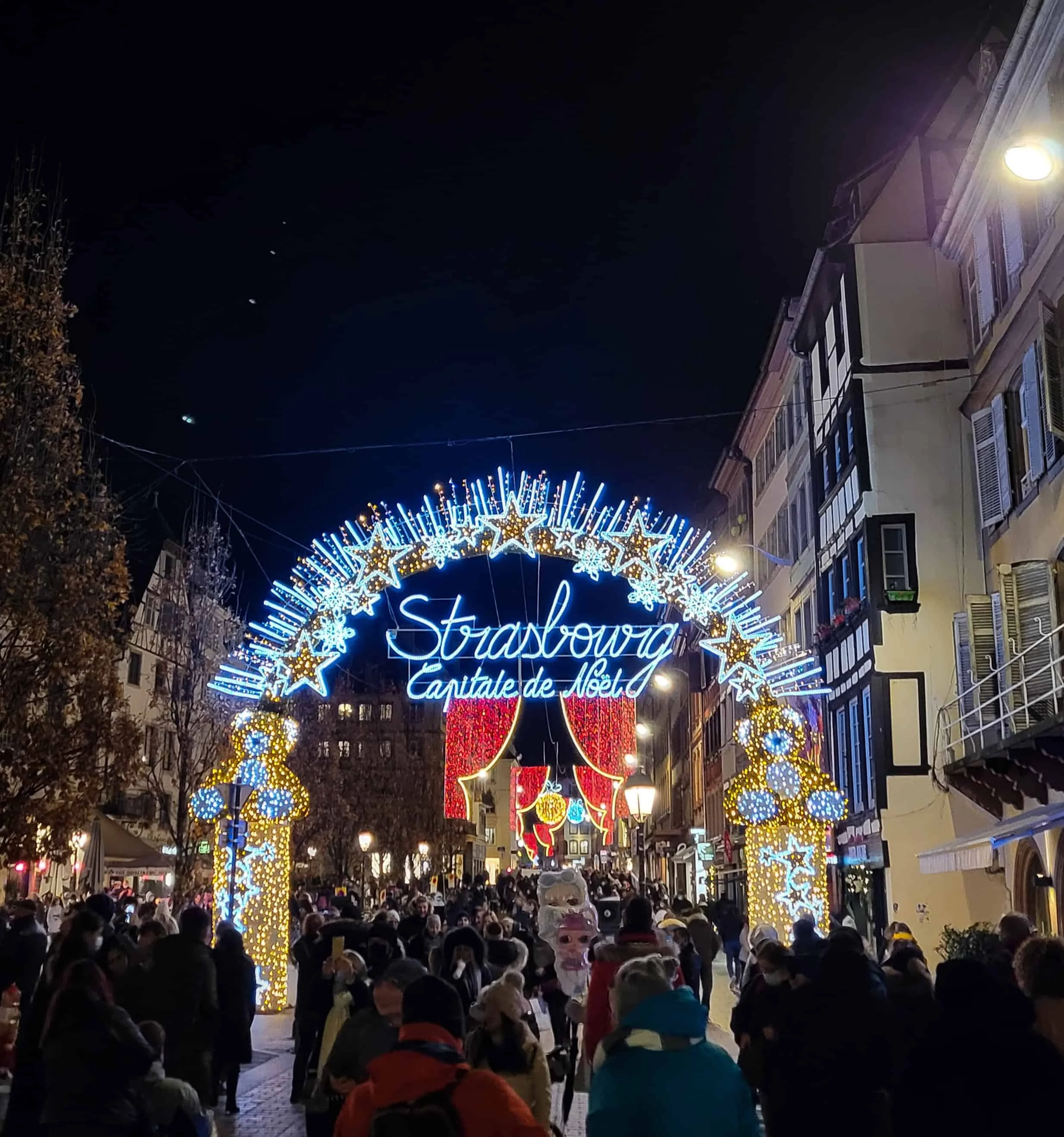 Lit arch reading Strasbourg Capitale de Noël over a crowded street lined with half-timbered buildings