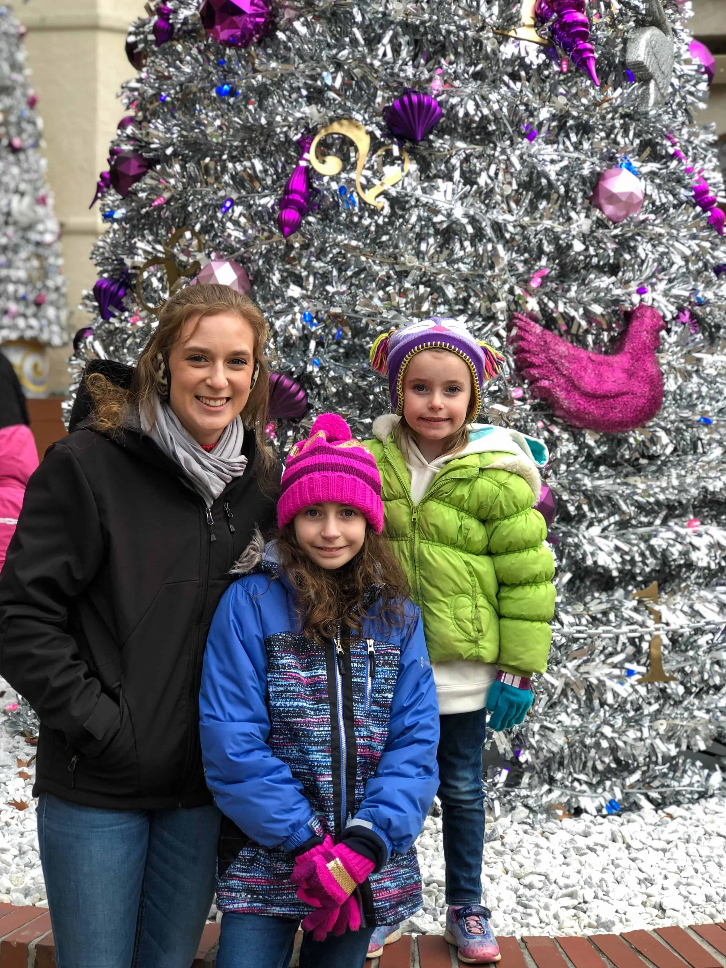 Three family members pose in front of a silver tinsel Christmas tree with purple ornaments and a pink bird ornament.