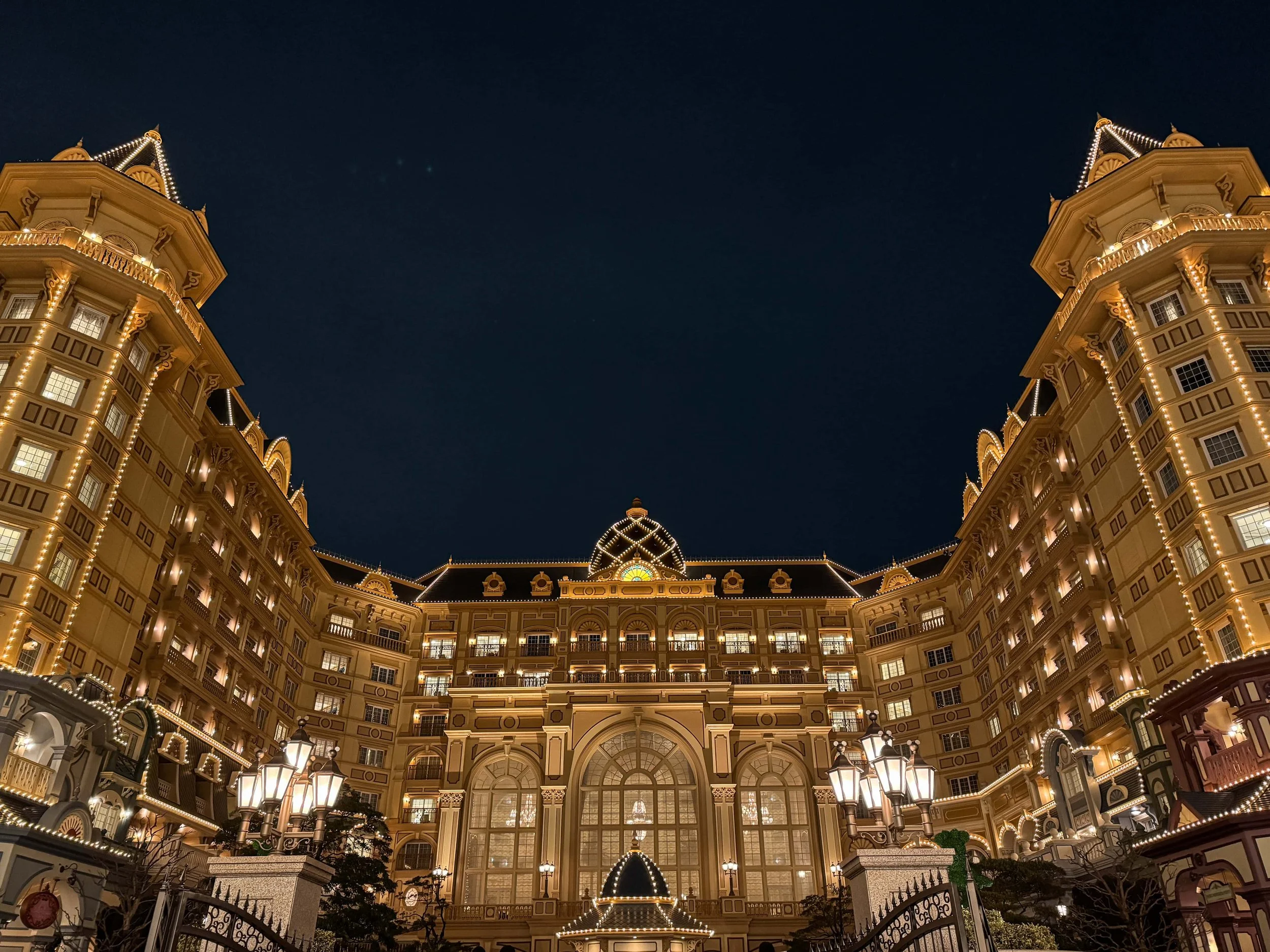 The Tokyo Disneyland Hotel glowing at night, its Victorian-style towers and arched windows outlined in golden lights