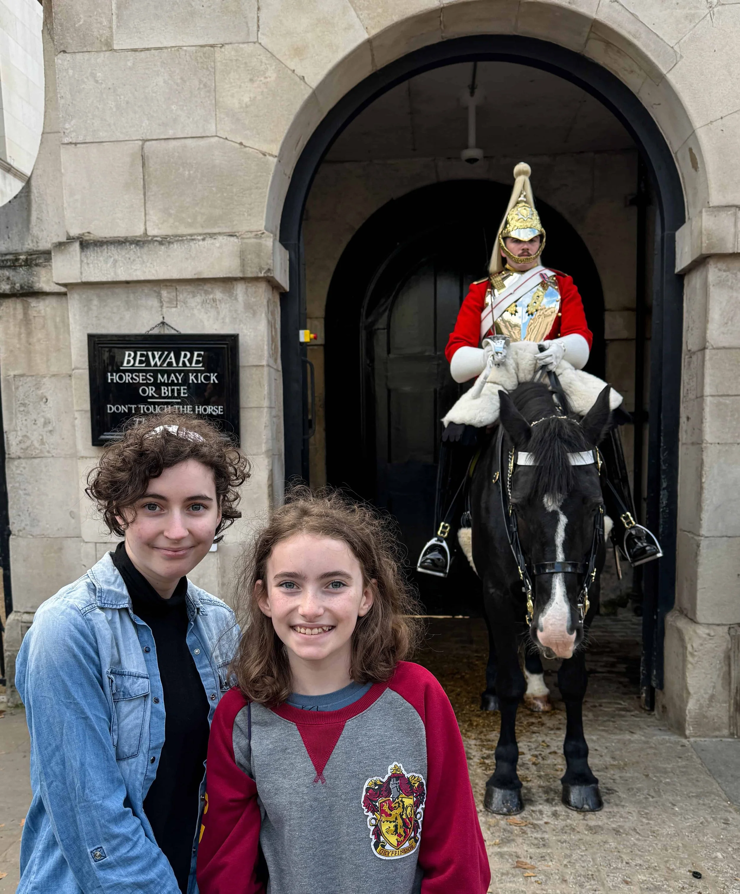 Two teenagers, Rachel and Sophie posing with a Household Cavalry mounted guard in ceremonial uniform at Buckingham Palace – memorable family moment in London.