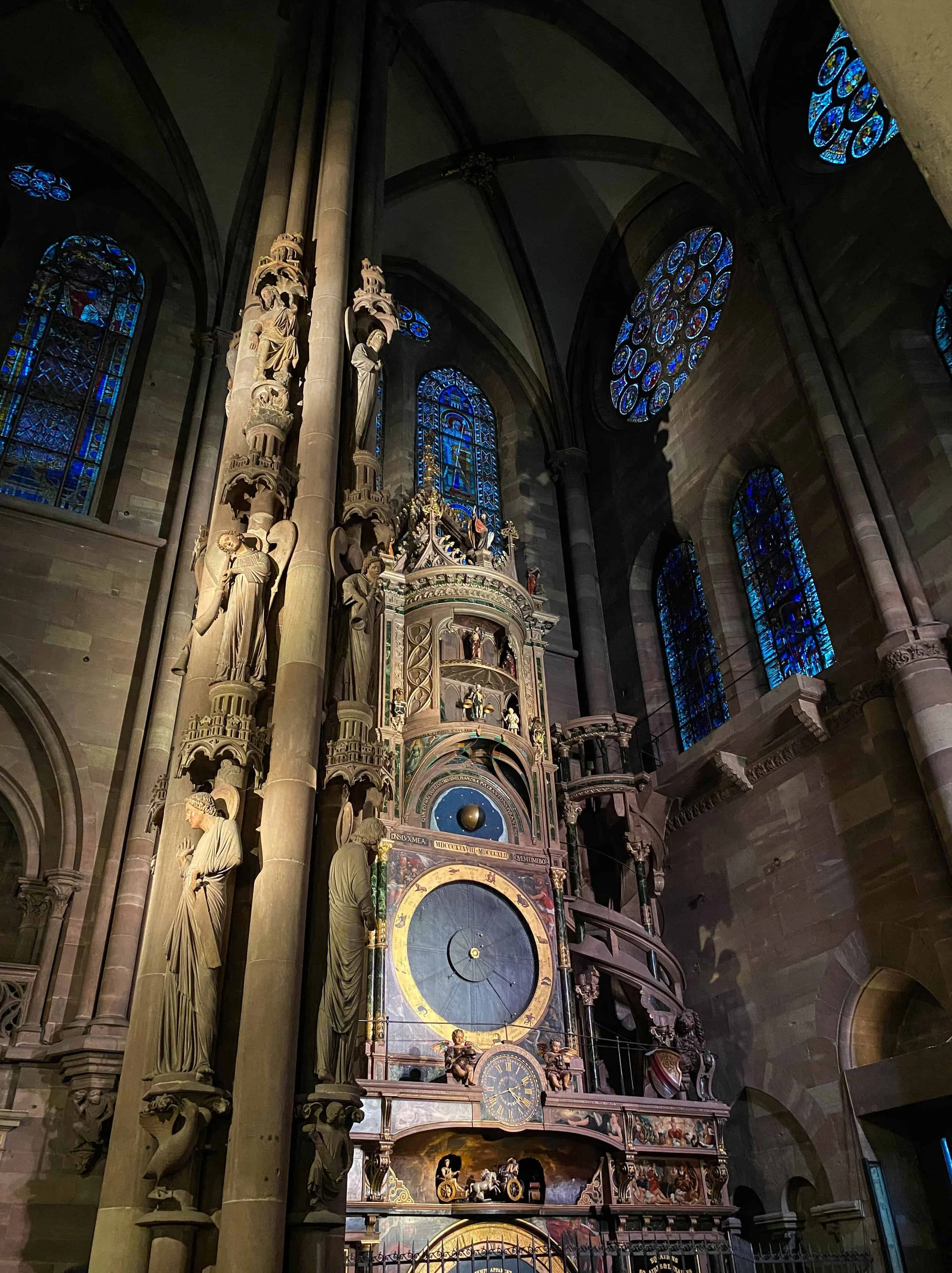 Ornate astronomical clock with statues and blue stained glass windows inside Strasbourg Cathedral