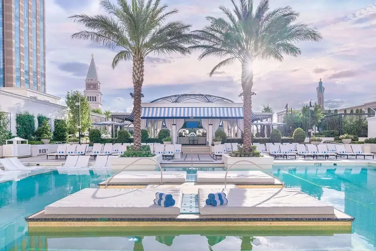 The Venetian Las Vegas pool deck with rows of white lounge chairs, palm trees, and the hotel's tower in the background.