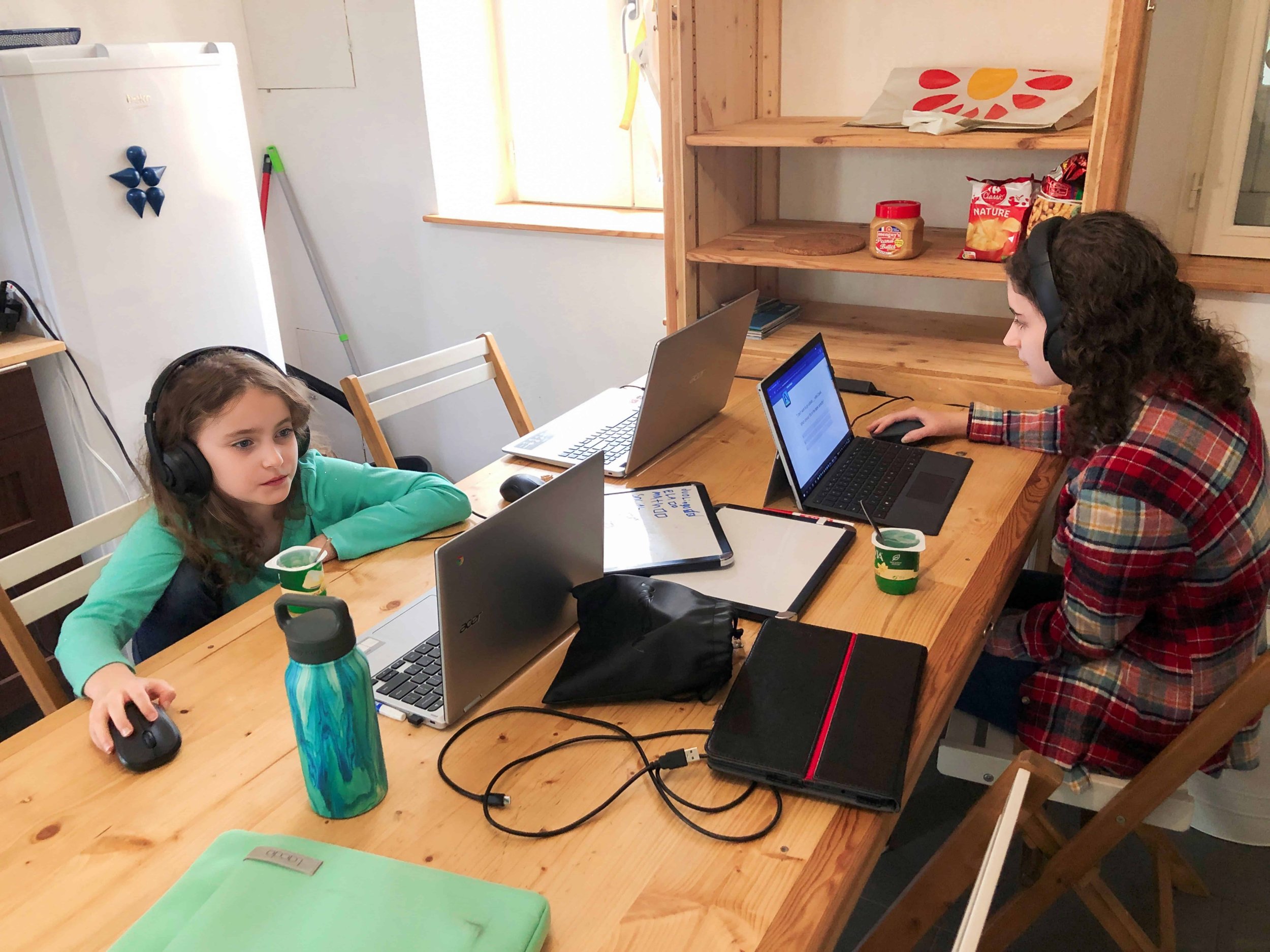 Two children engaged in homeschooling activities at a comfortable Airbnb rental in Étretat, France. They sit at a table with books, notebooks, and learning materials. The chose for authenticity over societal expectations.