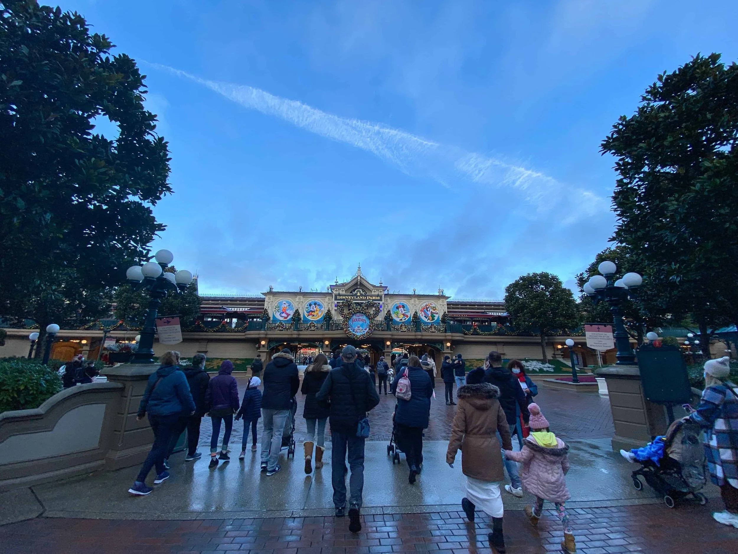 Visitors in winter coats walk toward the Christmas-decorated Main Street Station building inside Disneyland Park.