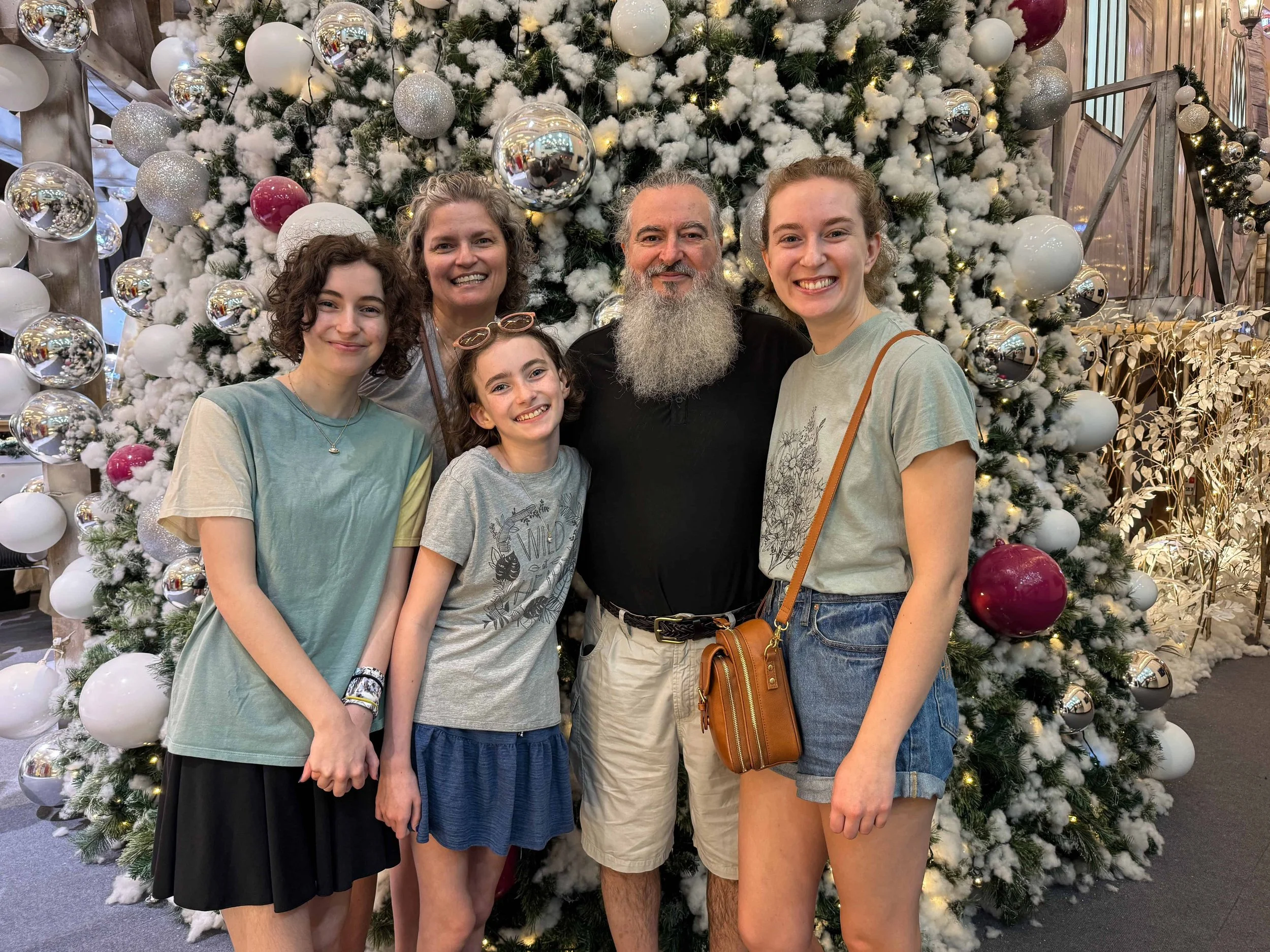 Five family members smile together in front of a flocked Christmas tree with silver and burgundy ornaments