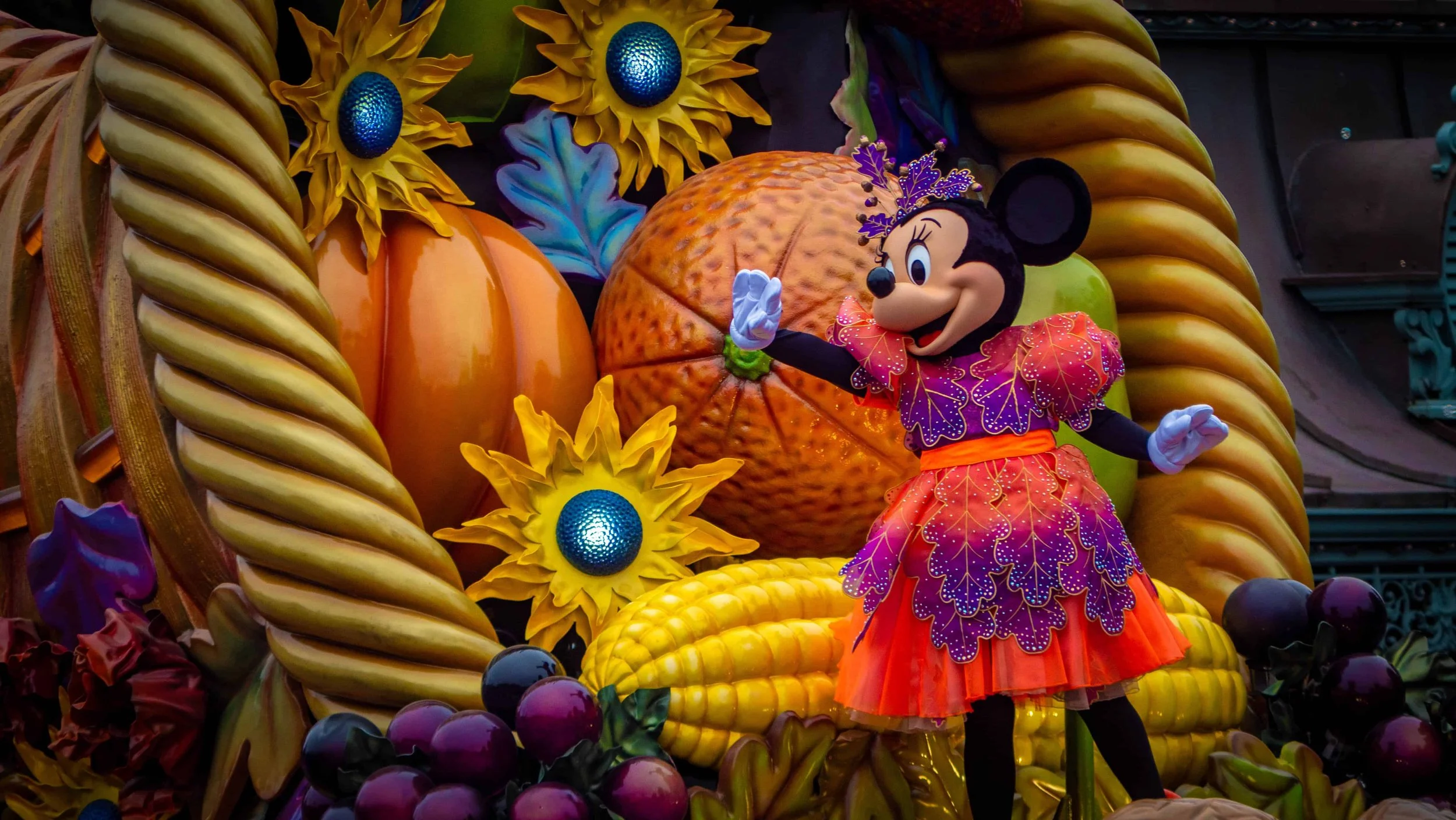 Minnie Mouse in a purple and orange autumn-themed costume on a harvest-decorated float during the Disneyland Paris Halloween parade.