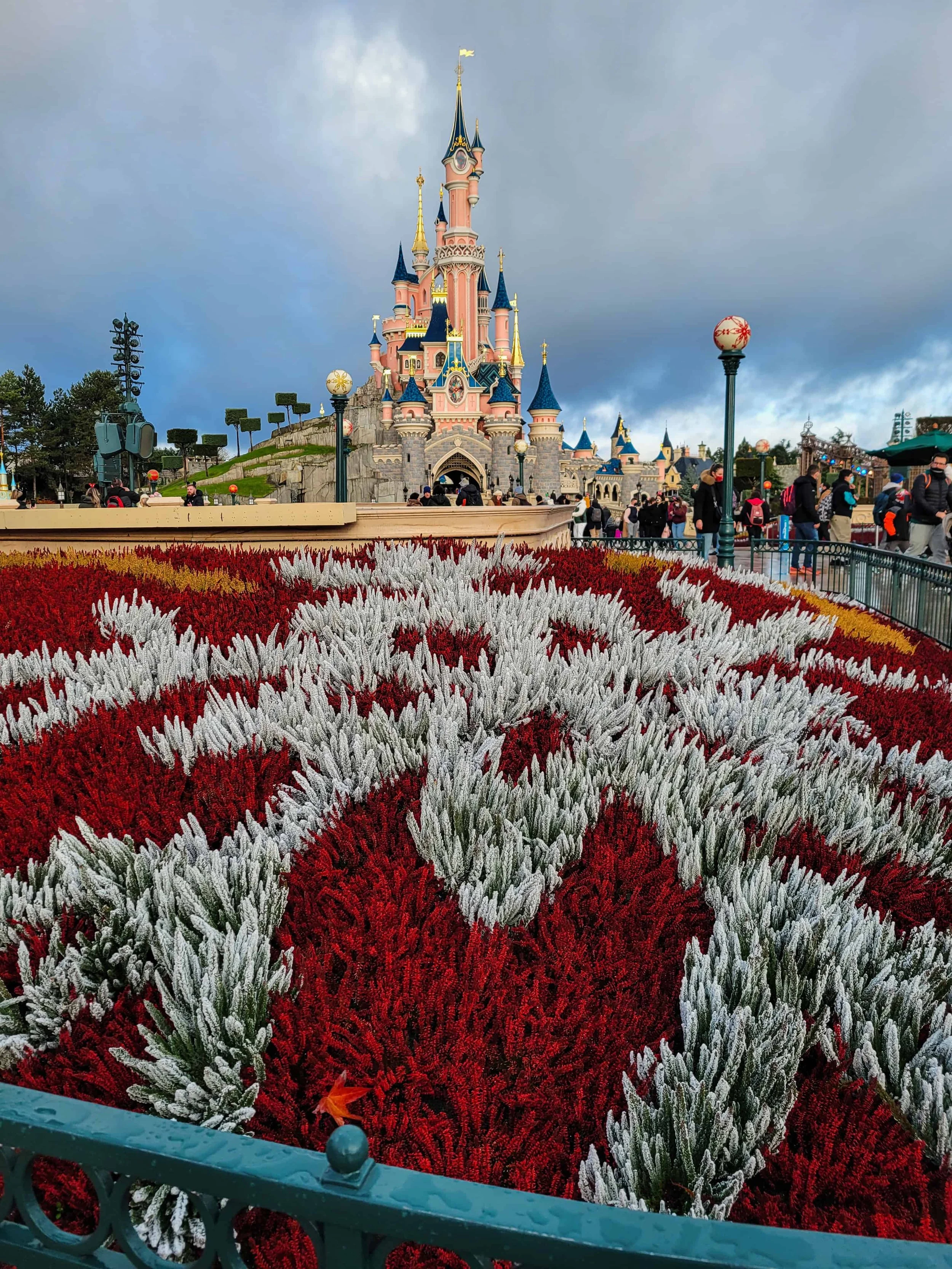 Sleeping Beauty Castle at Disneyland Paris behind a flower bed of red and white plants