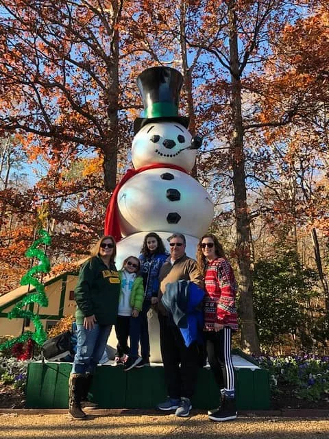 Five family members in winter clothes pose in front of a giant snowman with a top hat and red scarf at Christmas Town.