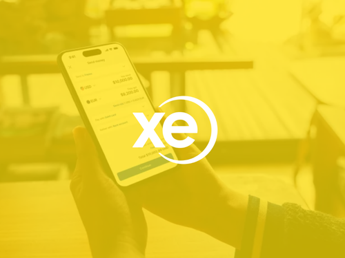 Person holding smartphone displaying a financial app with the XE currency exchange logo overlayed