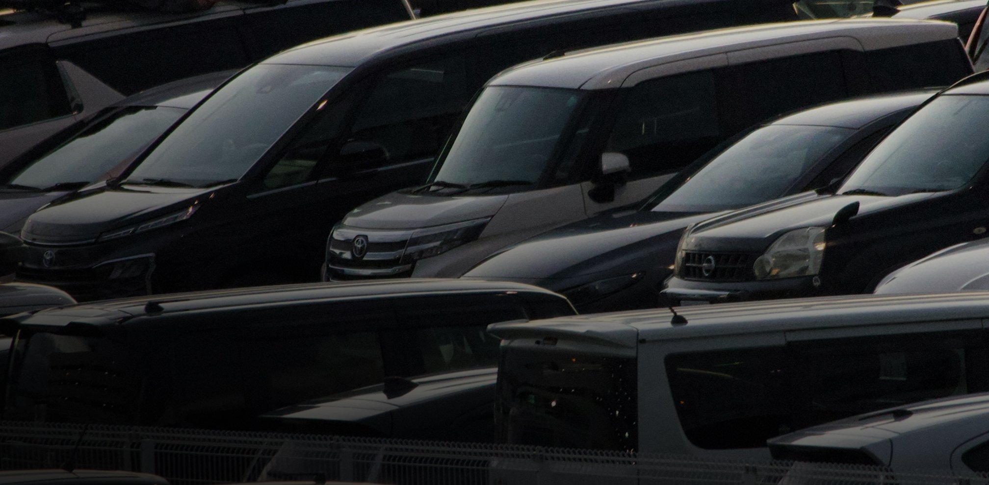 Close-up of multiple black and dark-colored cars parked in a parking lot, viewed from above.