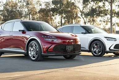 Red and white SUVs parked side by side on a paved surface with trees in the background.
