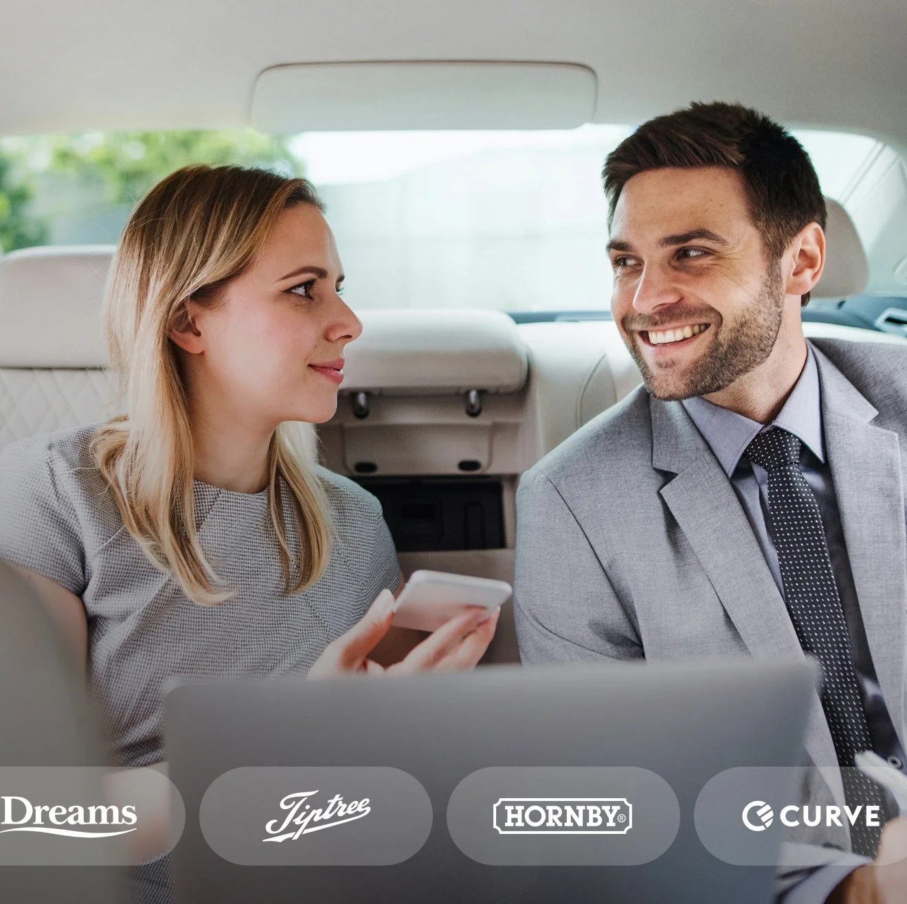 A woman and a man in formal attire sitting in the backseat of a car, engaging in conversation, with the woman holding a smartphone.