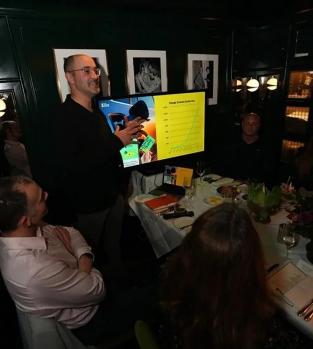 Man giving presentation on a large screen at a restaurant with seated dining guests.