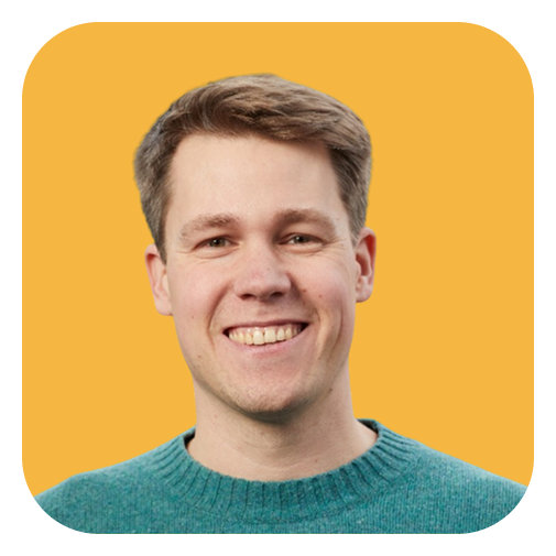 A smiling young man with short light brown hair, wearing a teal sweater, against a yellow background.