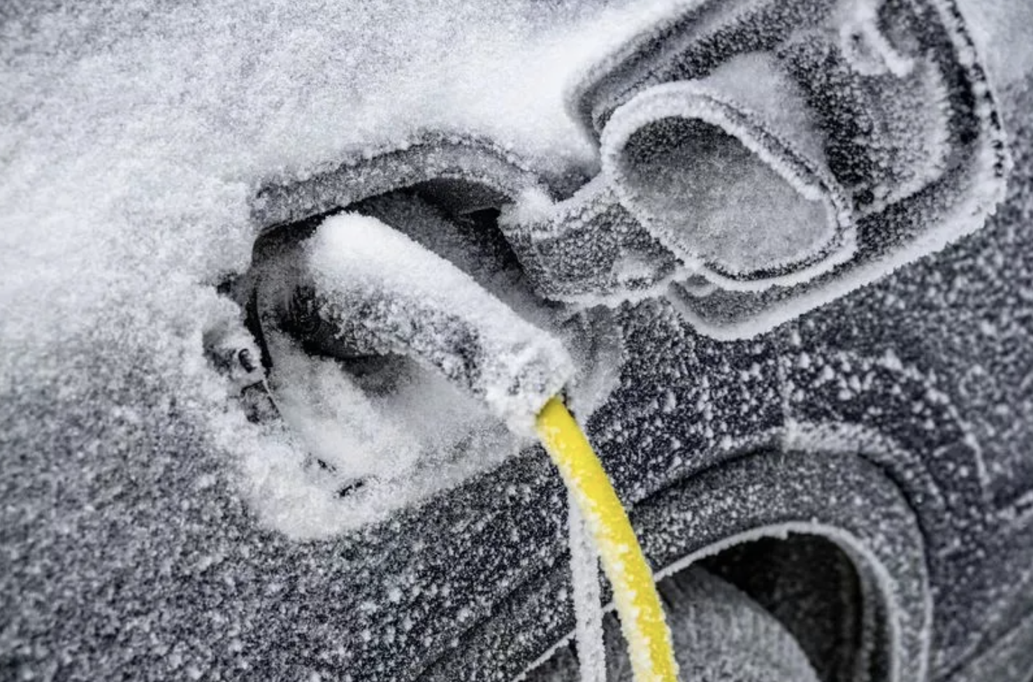 Close-up of a snow-covered electrical outlet with a yellow extension cord plugged in.