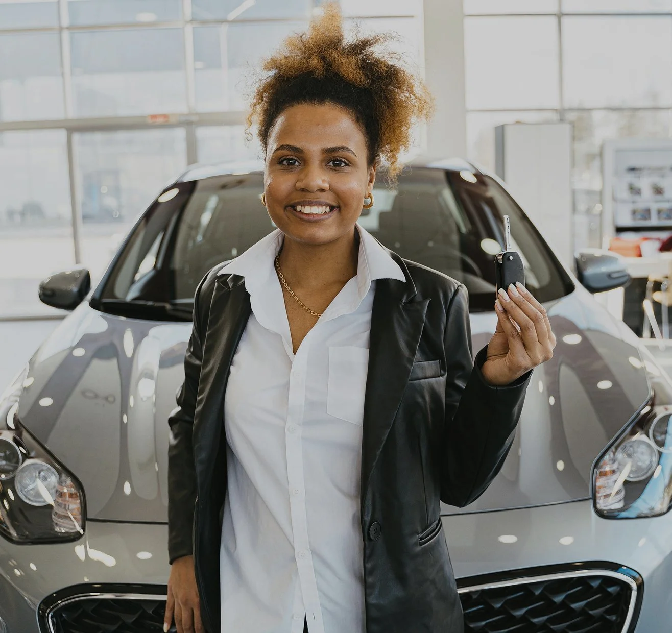 A woman holding car keys at a car dealership showroom.