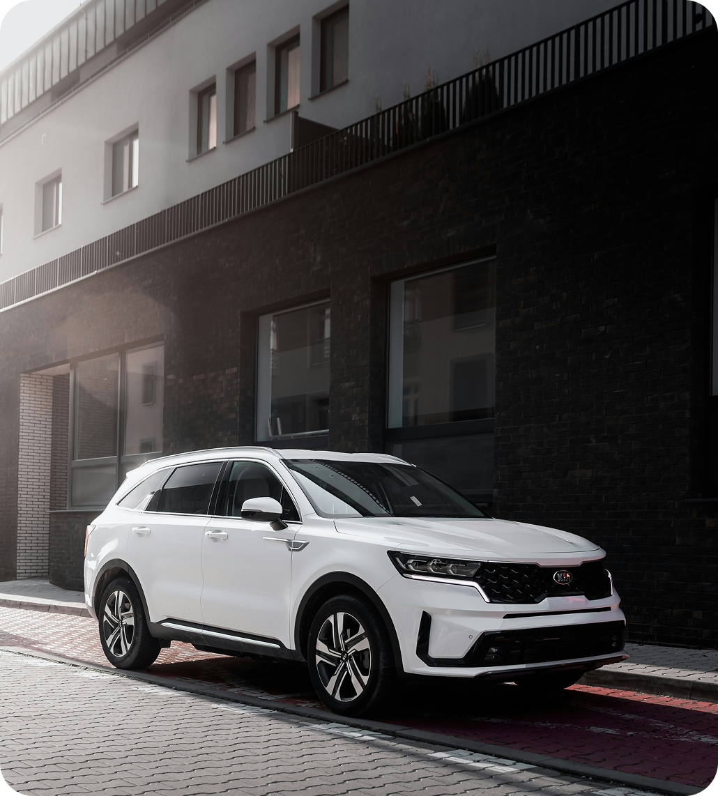 A white SUV parked on a city street next to a modern building with black brick and large windows.