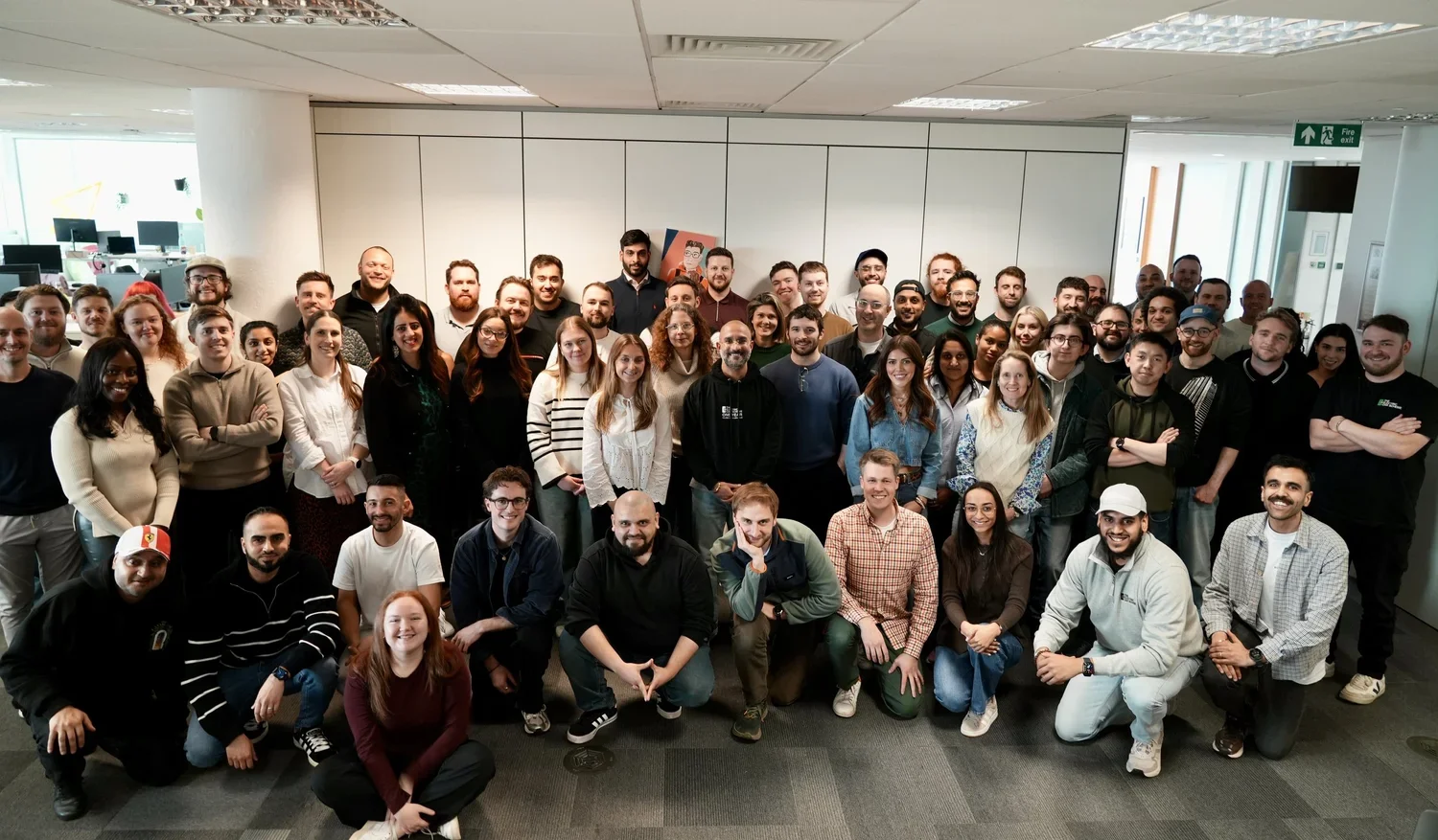 Group photo of many diverse people in an office environment, standing and kneeling, smiling at the camera.