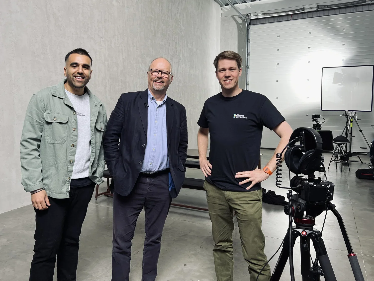 Three men standing in a studio with camera equipment and lighting, smiling at the camera.
