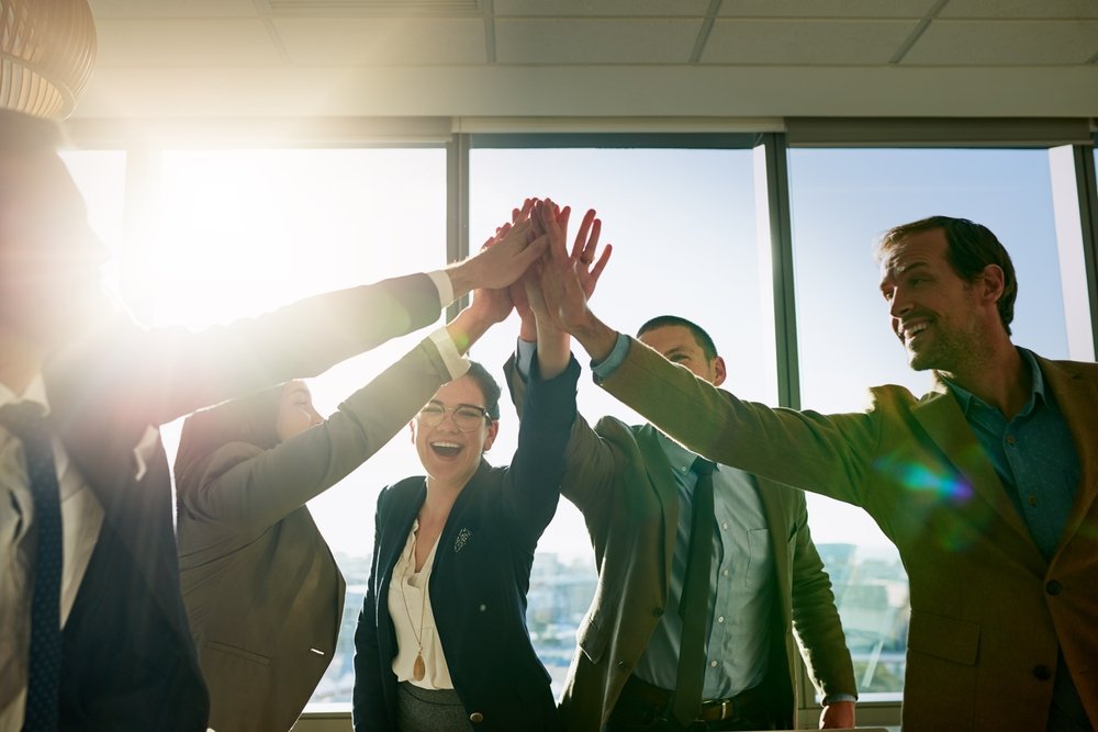 Business team celebrating and giving high-fives in an office with large windows and sunlight